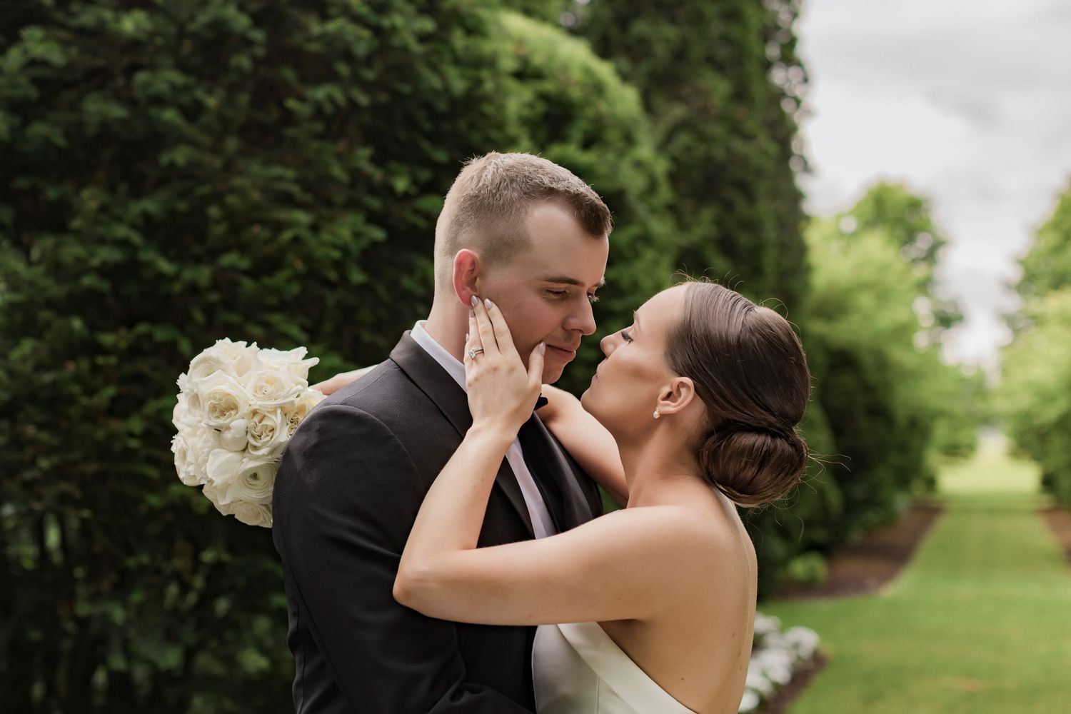 Romantic wedding moment captured in lush garden setting with white bouquet.