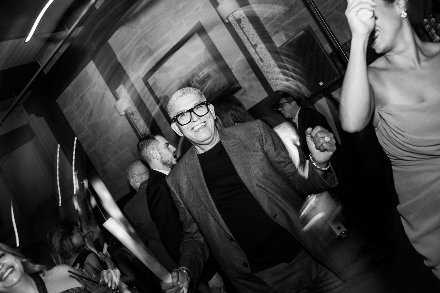 Party guests dancing and celebrating in black and white on a dimly lit dance floor.