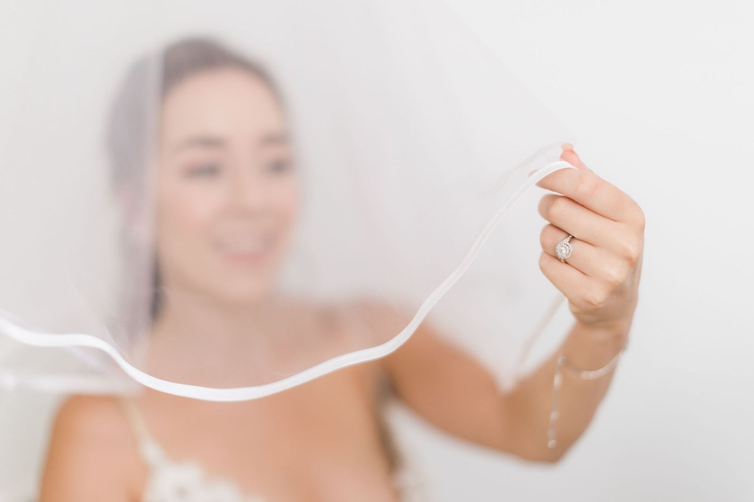 A soft focus artistic wedding detail photo showing a delicate veil being held against a light background.