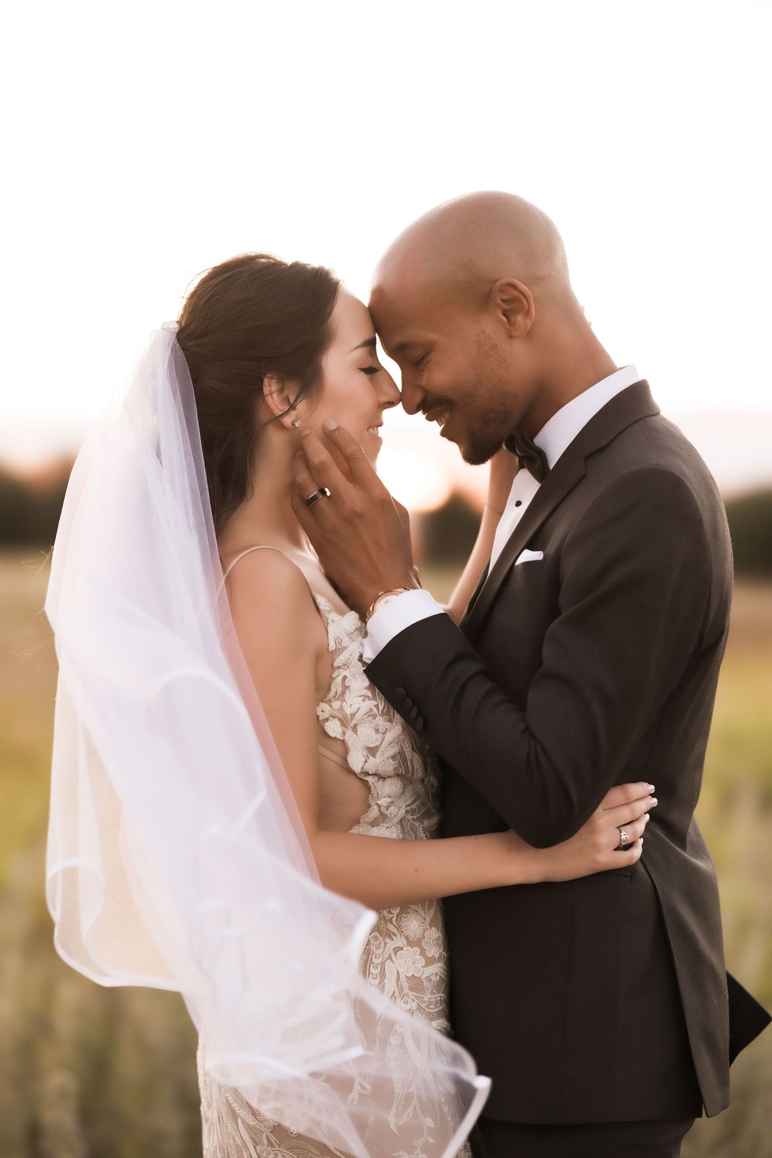 A romantic wedding portrait showing a tender moment between newlyweds at sunset.