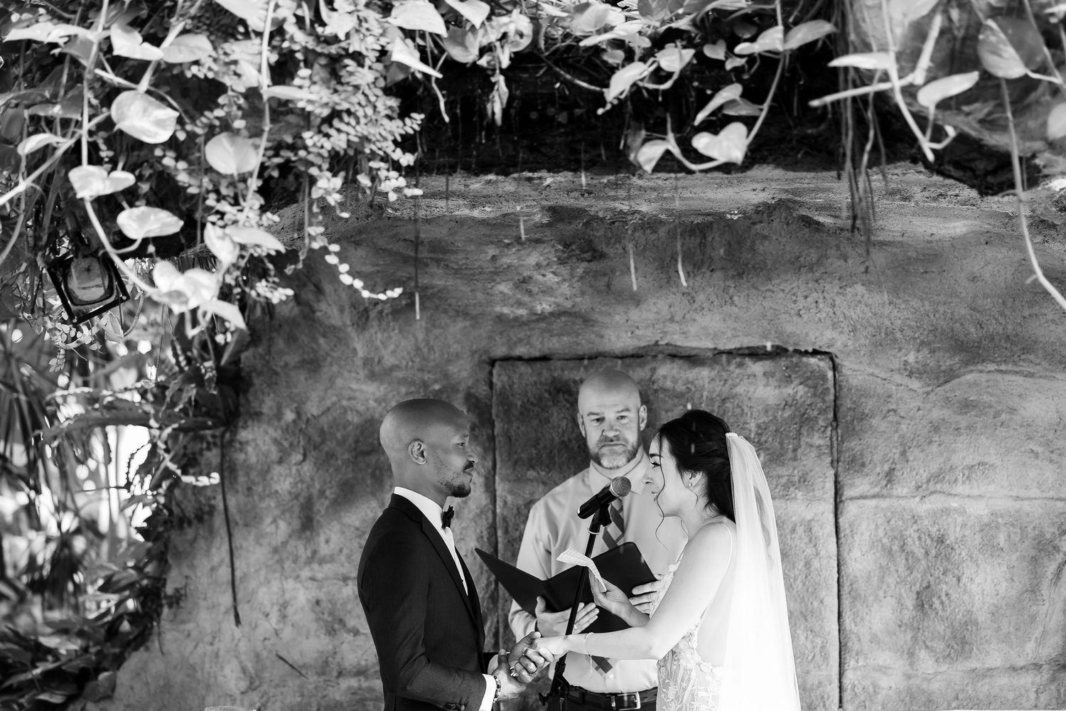 Black and white photo of wedding ceremony in rustic stone alcove with floral decorations.