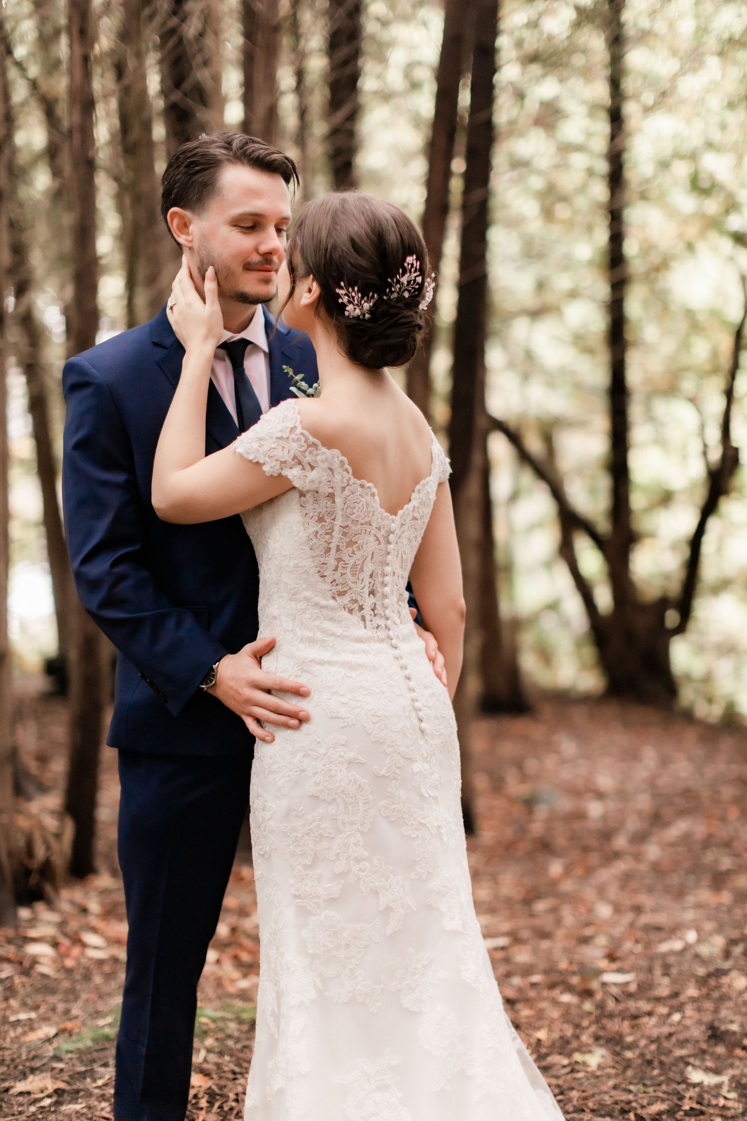 A tender wedding moment captured in a forest with fall foliage and soft lighting.