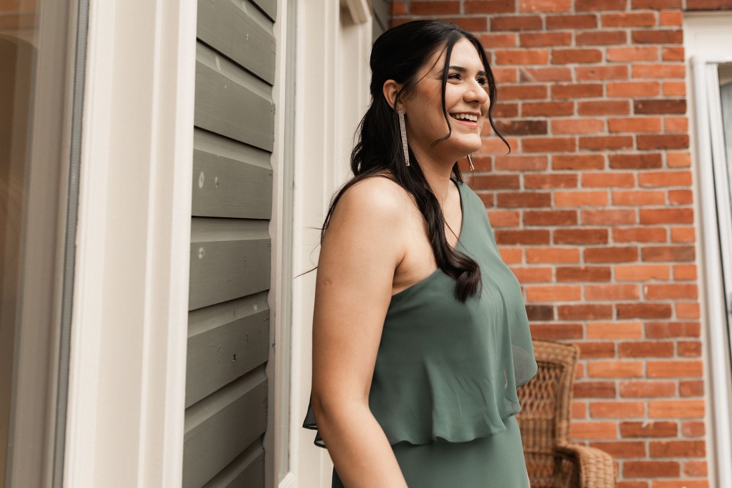 Person in green flowing top smiling while standing by brick exterior wall.