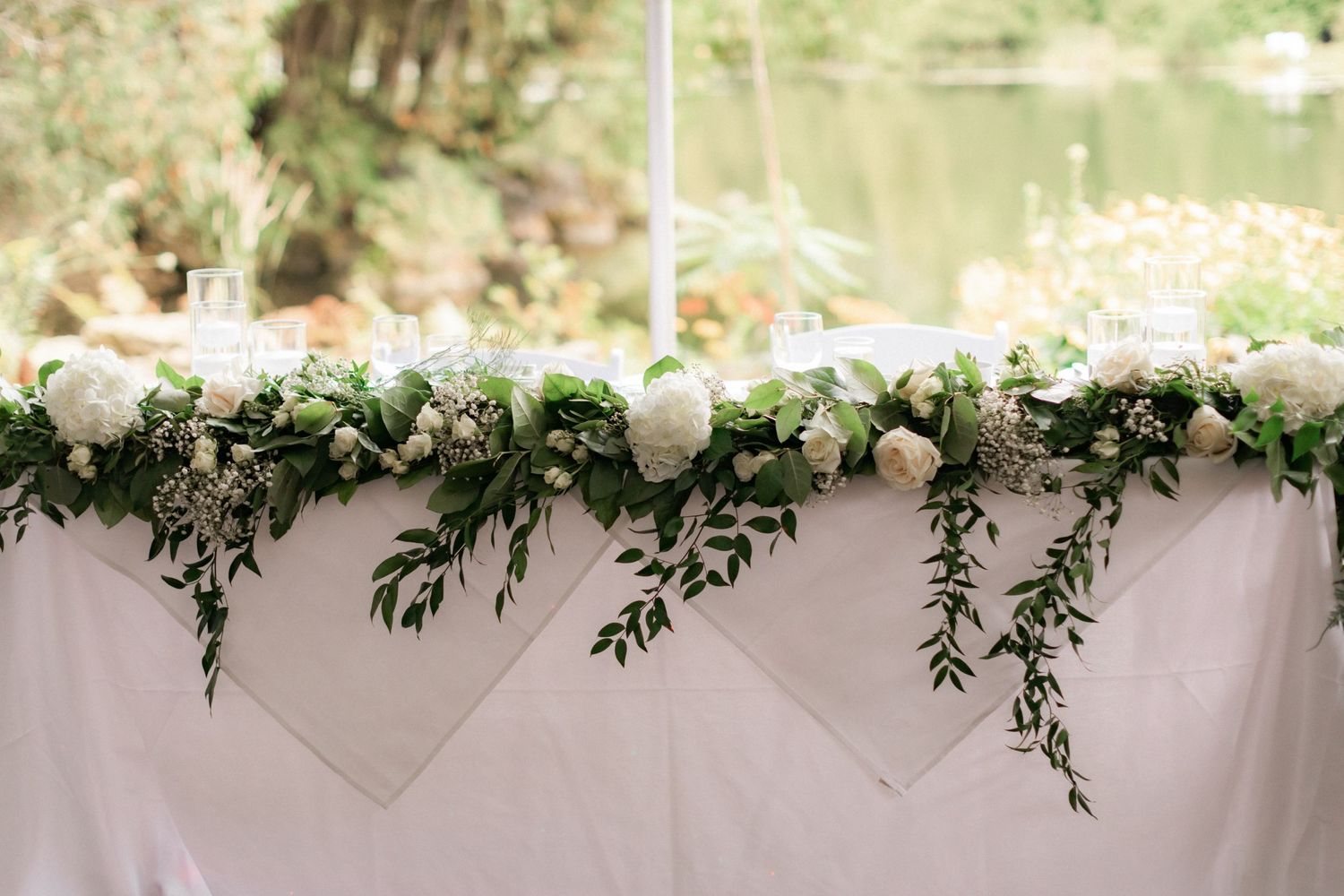 White floral and greenery garland decorates wedding reception table.