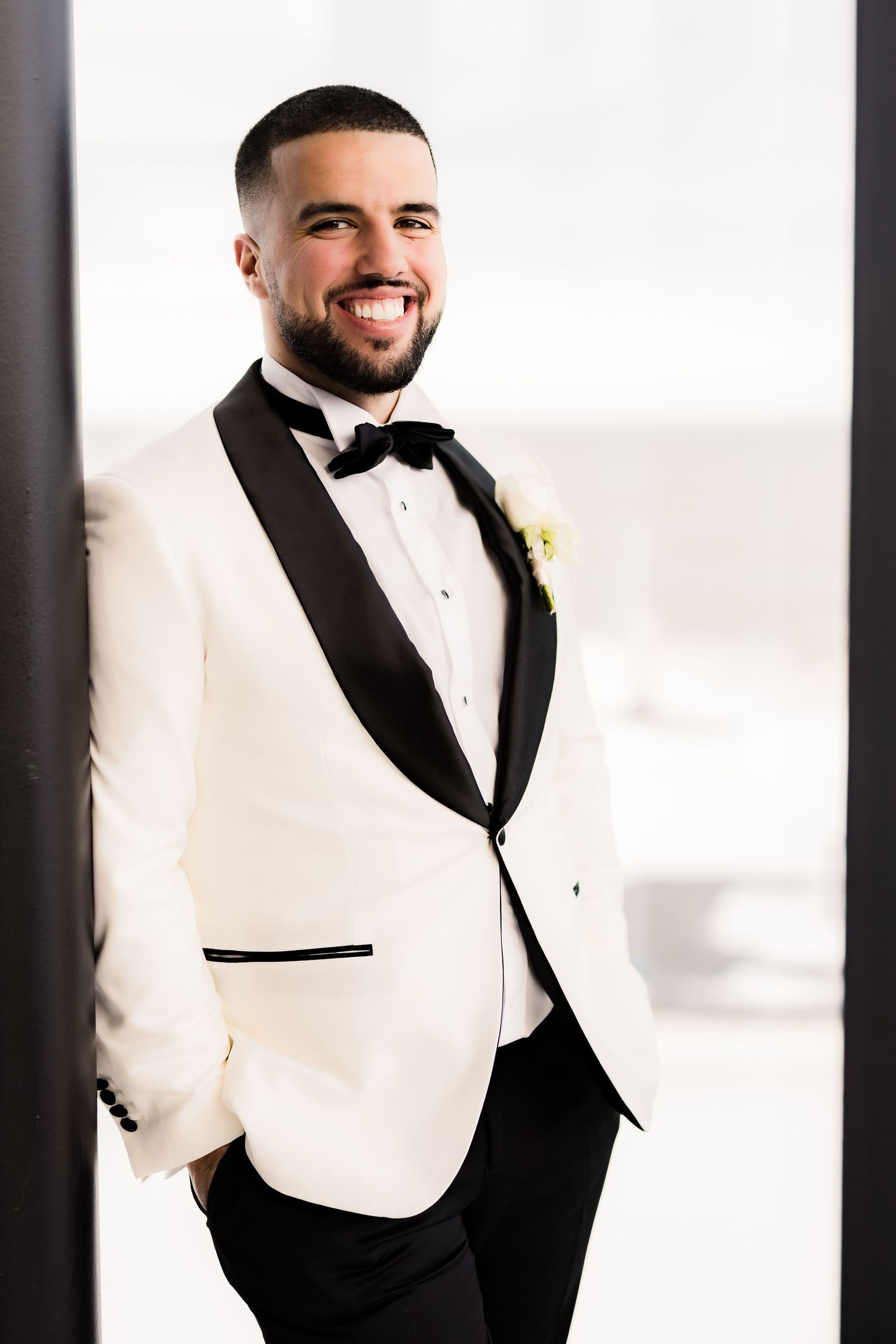 Groom in classic white dinner jacket smiles during wedding portraits.