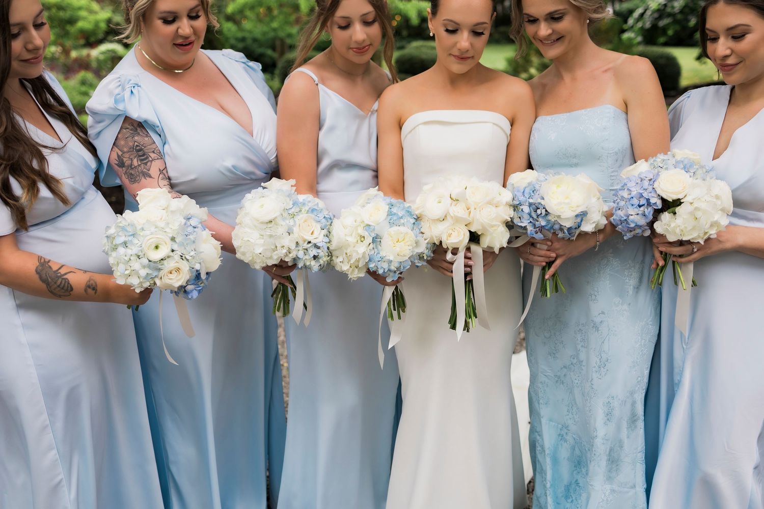 A row of bridesmaids in light blue dresses holding white floral bouquets at a wedding ceremony.