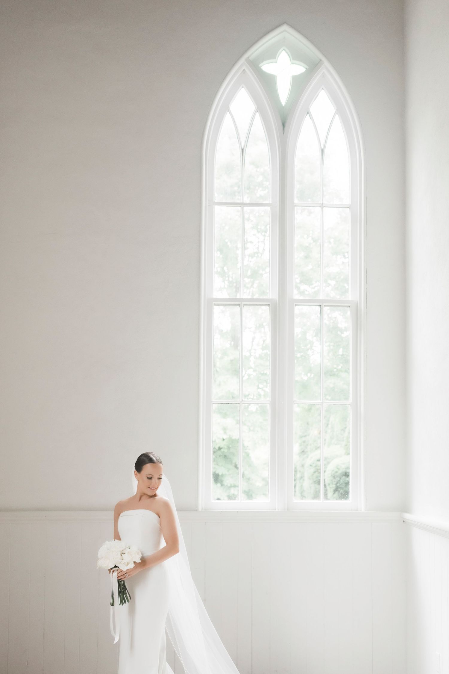 A bright white chapel interior with elegant arched Gothic windows creates a serene bridal portrait setting.