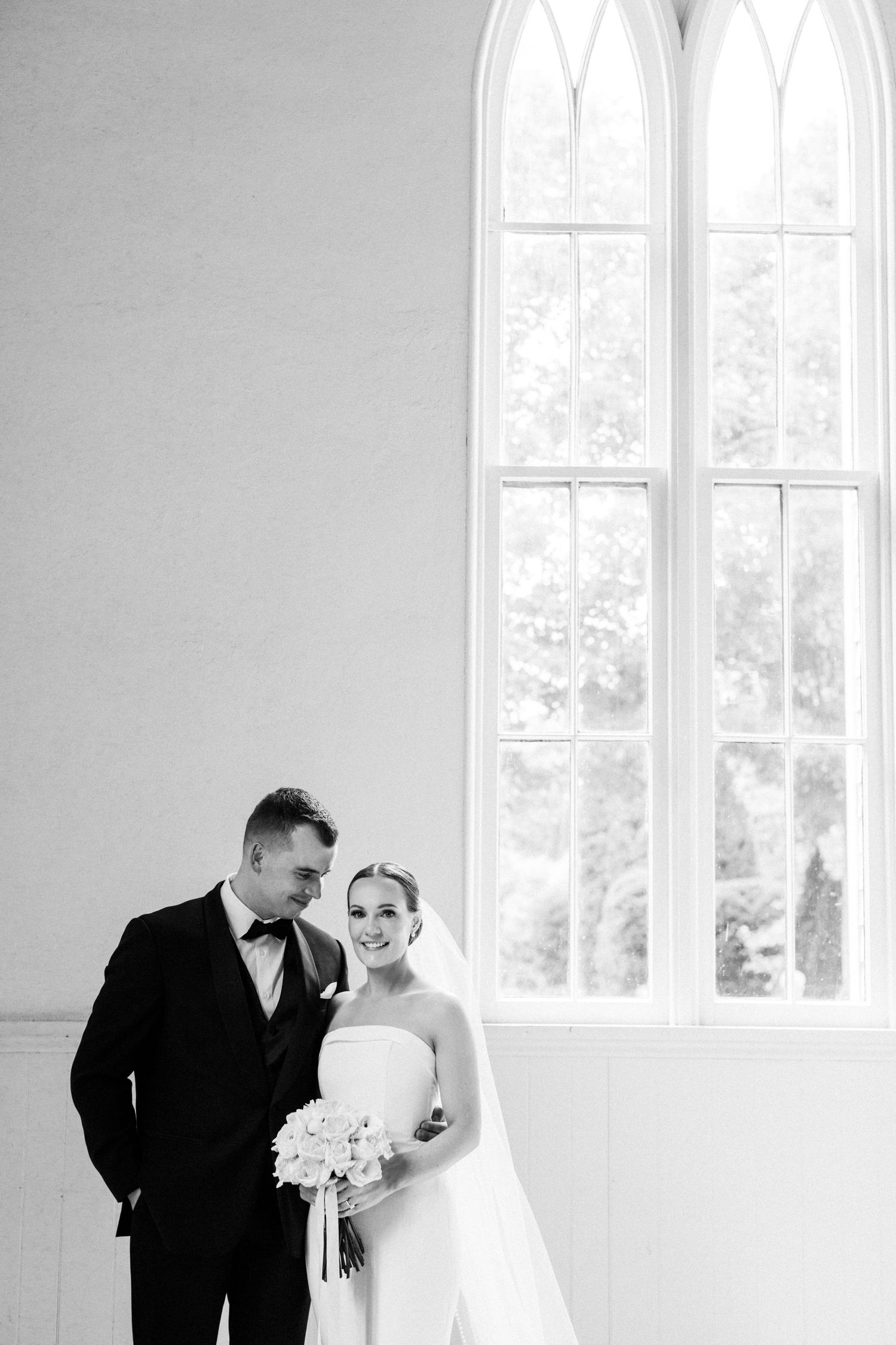 Classic black and white wedding portrait with dramatic arched church windows.