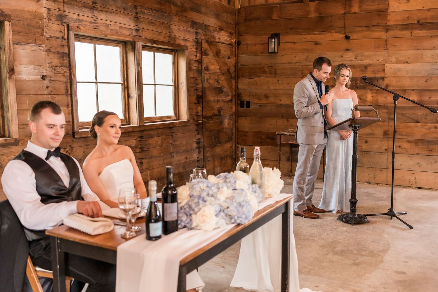 Wedding reception inside rustic wooden cabin with head table setup and speakers at microphone stand.