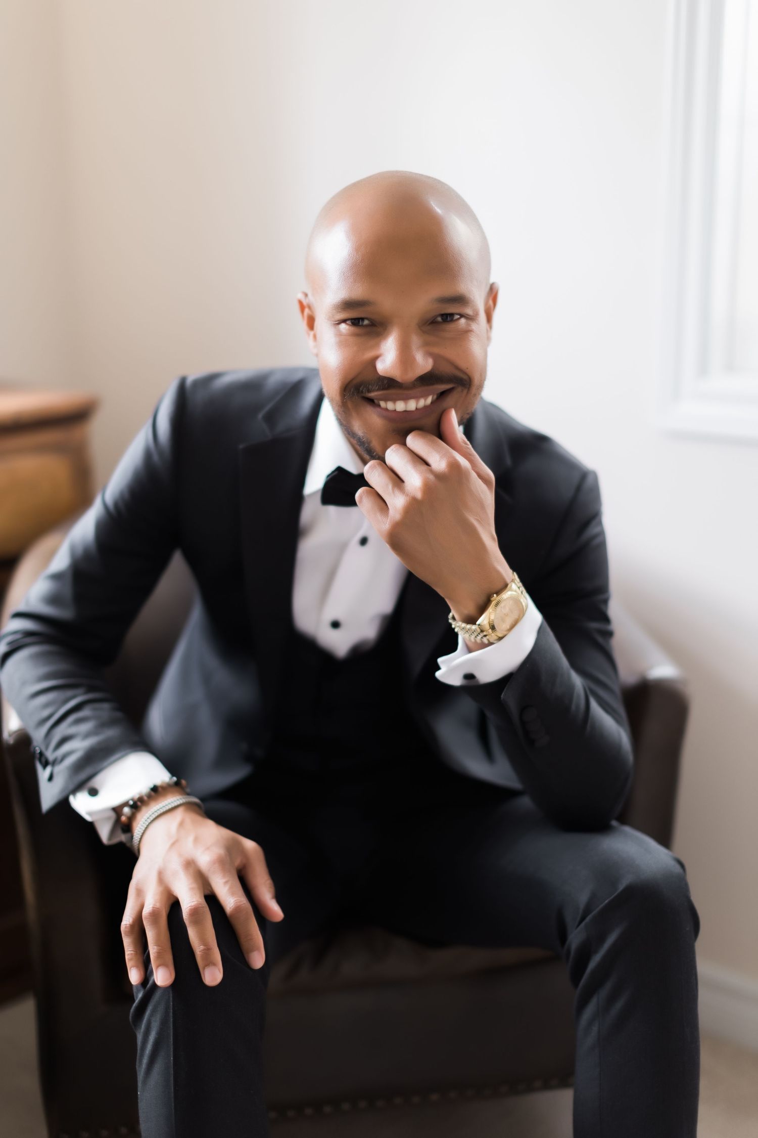 Stylish portrait of person in tuxedo seated in brown leather chair with warm lighting.