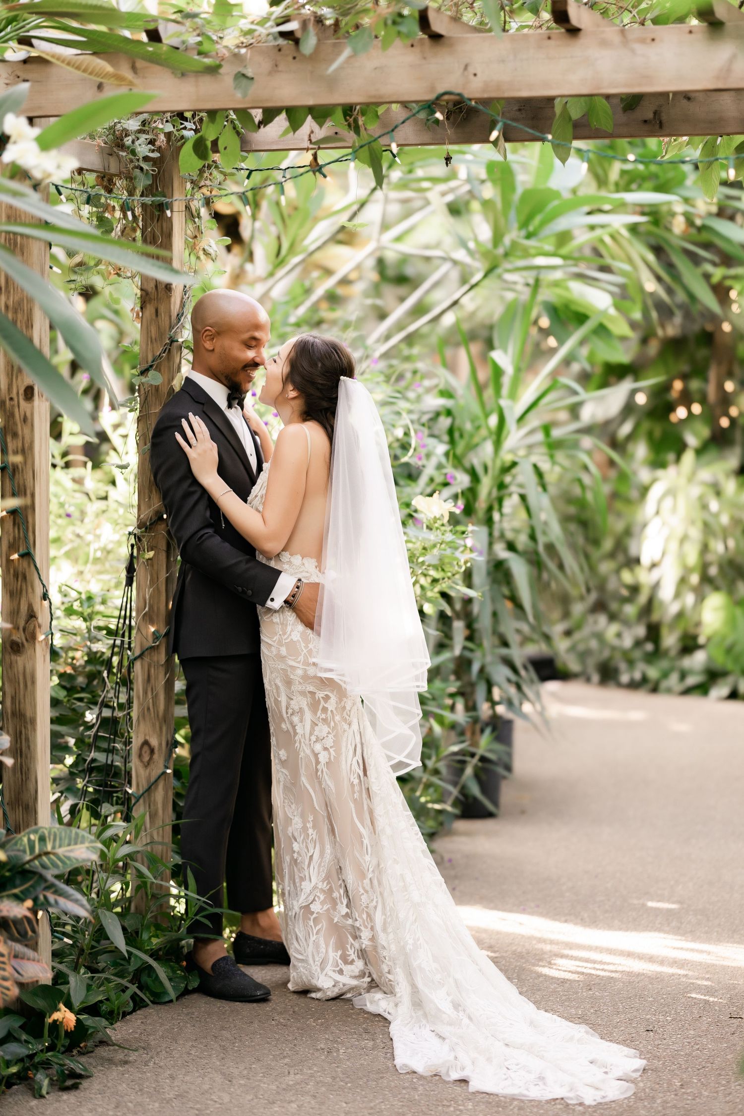 A tender embrace between newlyweds under a garden arbor surrounded by tropical foliage.