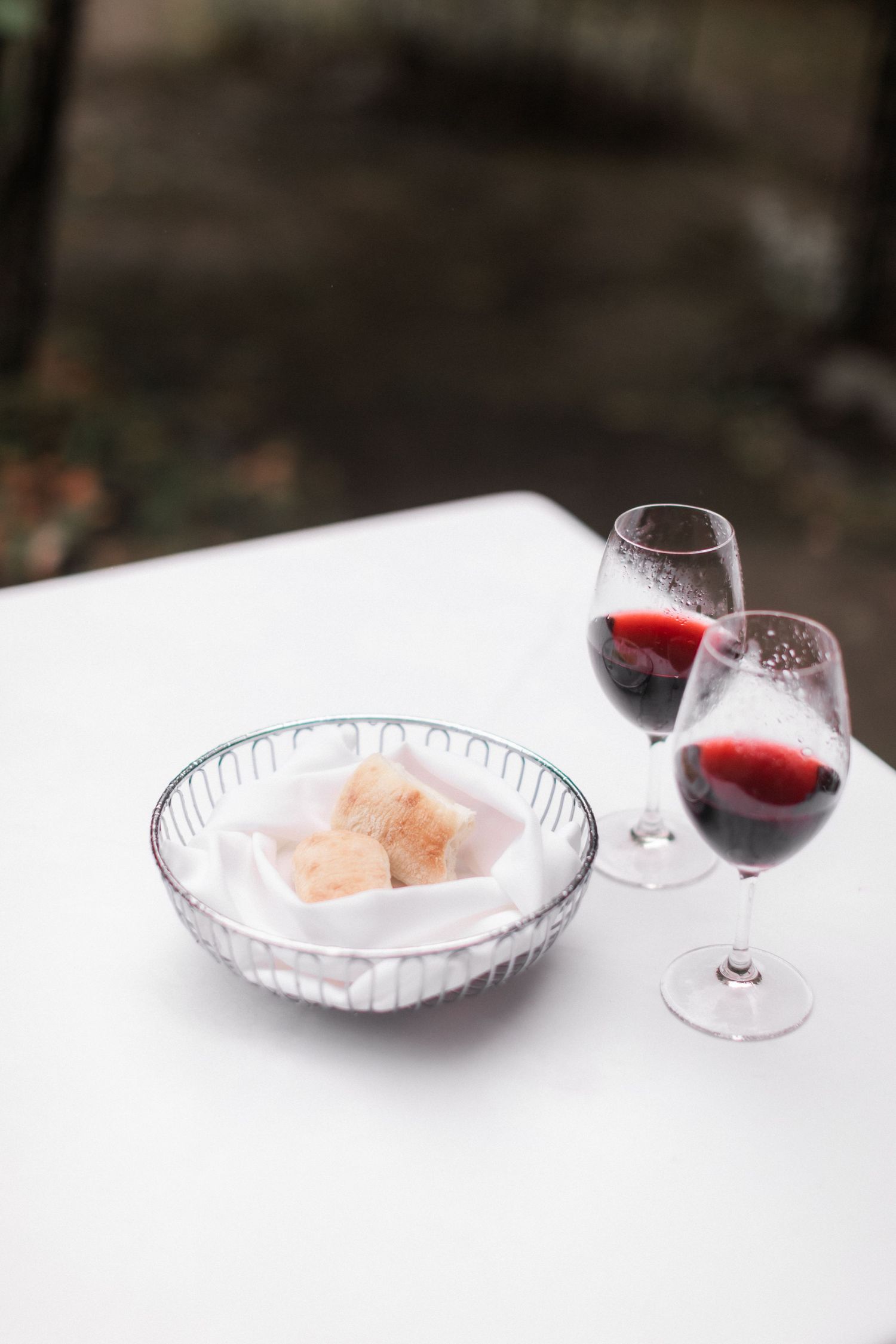 Two glasses of red wine beside a crystal bowl of appetizers on a white tablecloth.
