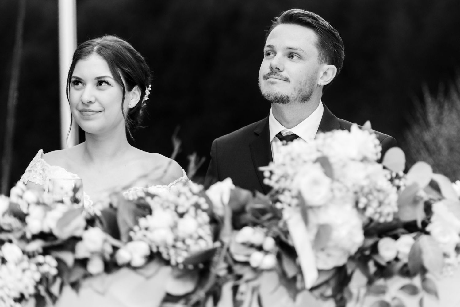 A black and white portrait of a couple seated at their decorated wedding reception table.