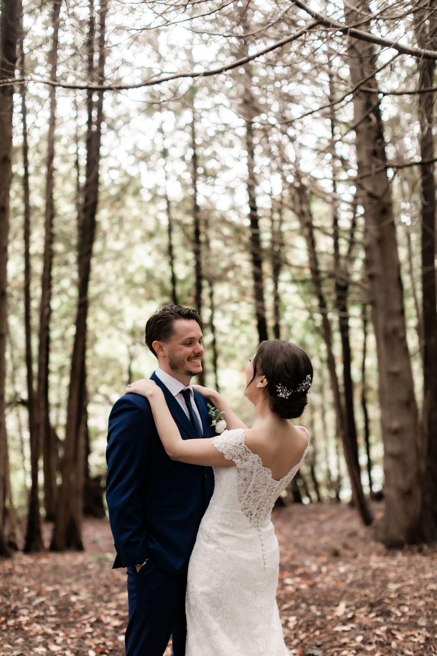 Romantic wedding couple embracing among tall trees on forest path.