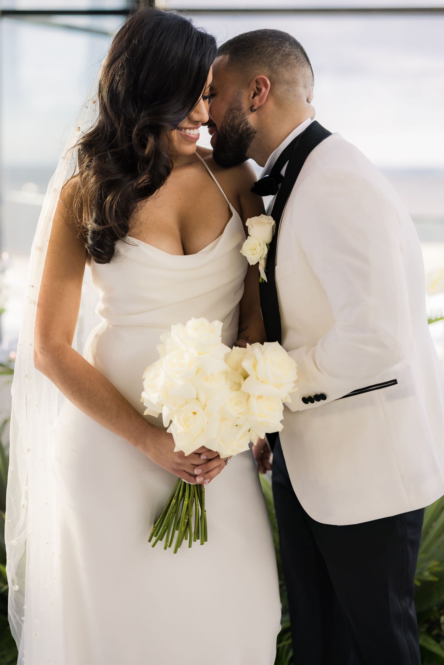 A tender moment between newlyweds with a cream bouquet and elegant white attire.