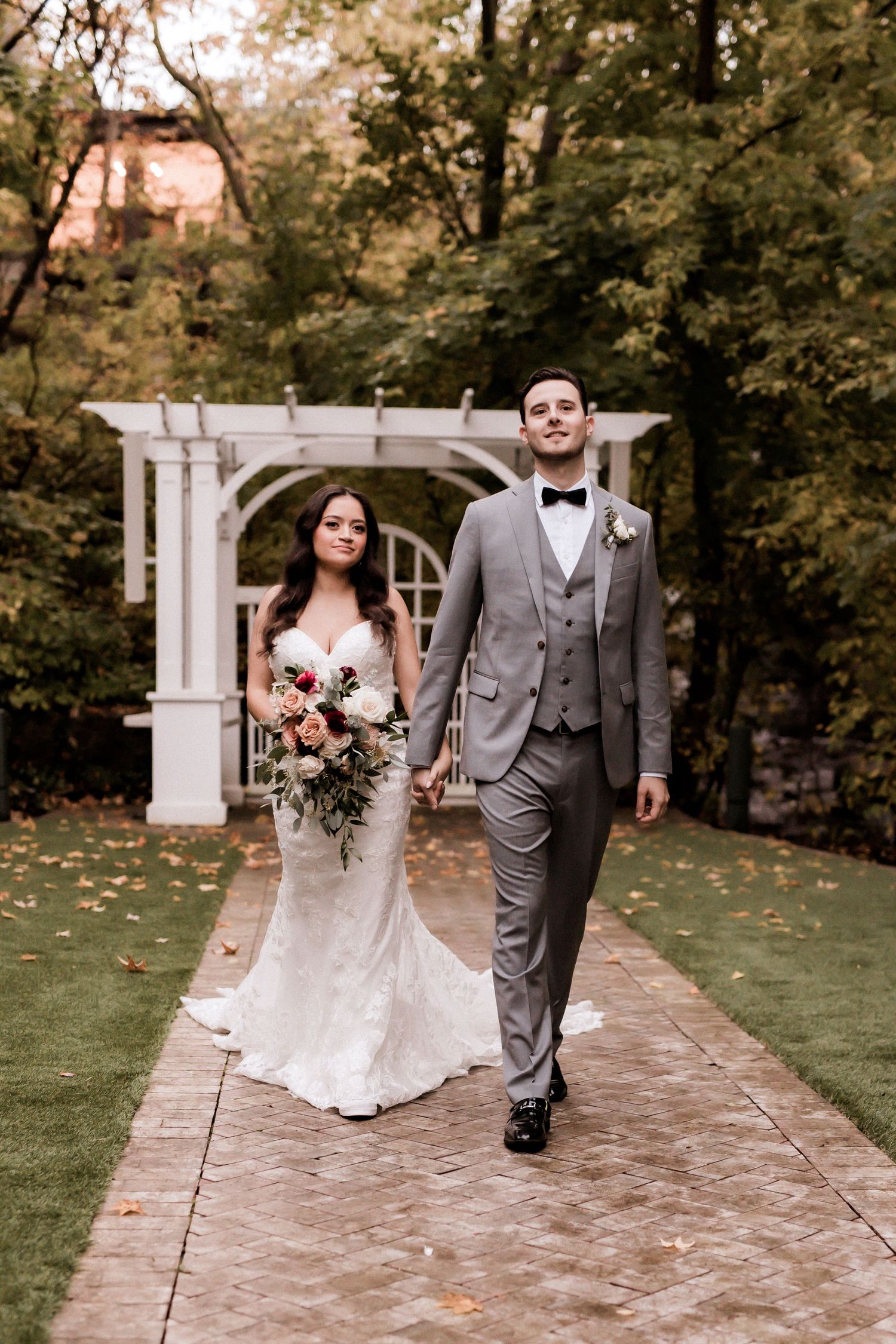 A couple walks hand in hand under a white garden arch in their wedding attire.