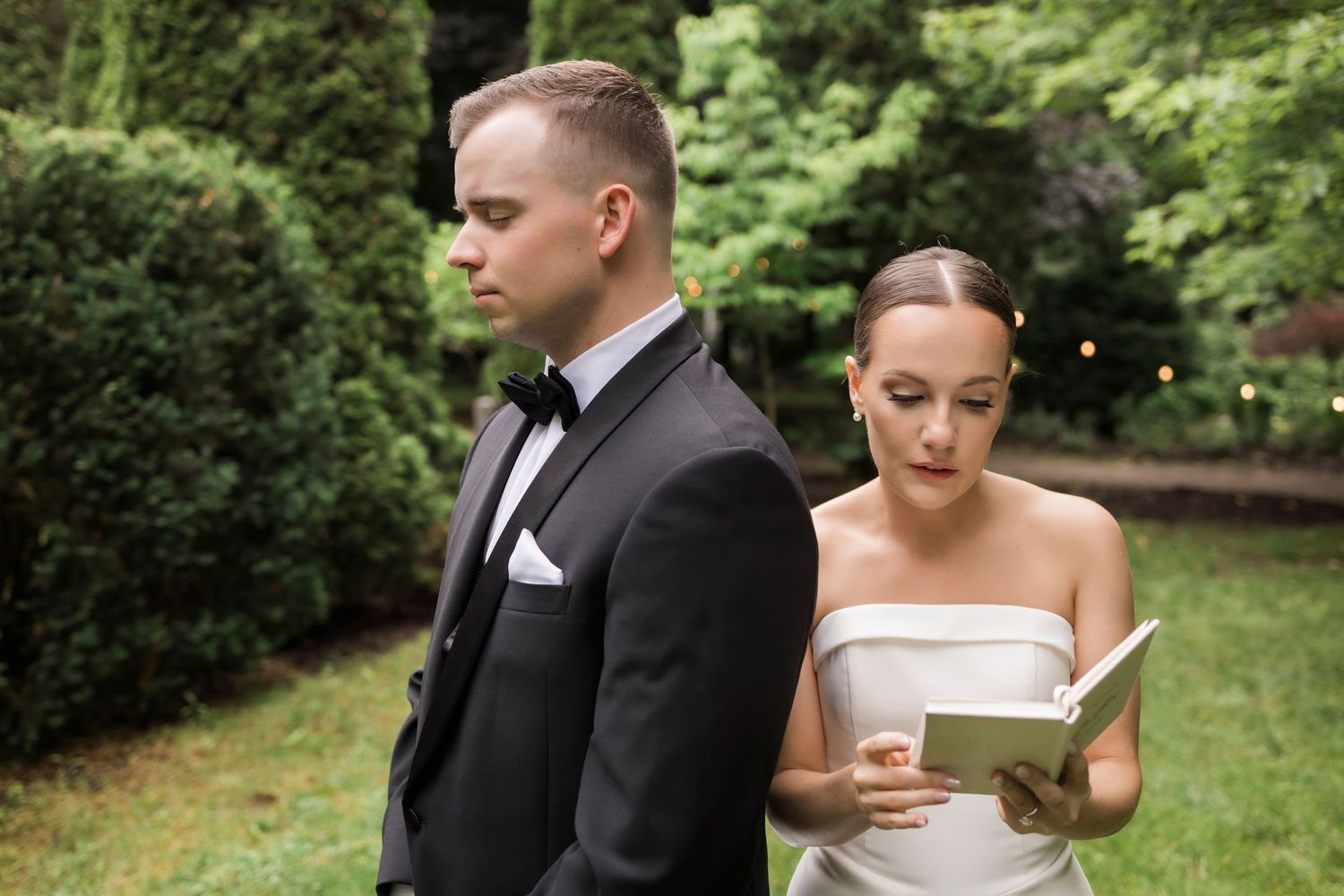 Wedding couple outdoors in a lush green garden setting reading notes from paper.