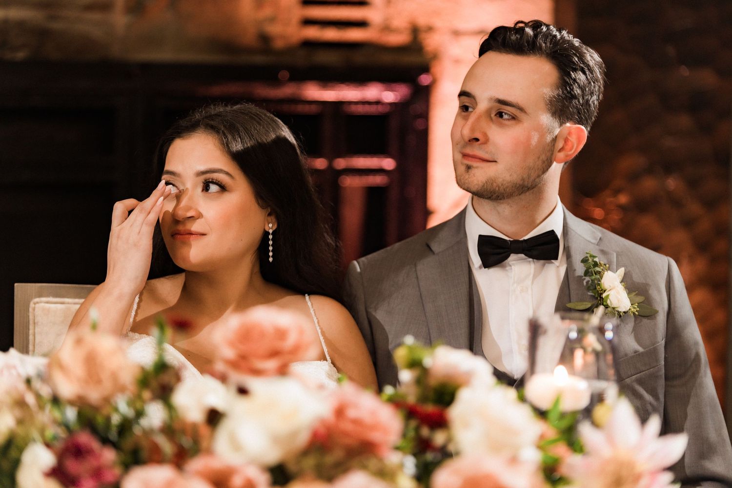 Wedding couple shares emotional moment during reception behind beautiful peach floral centerpiece.