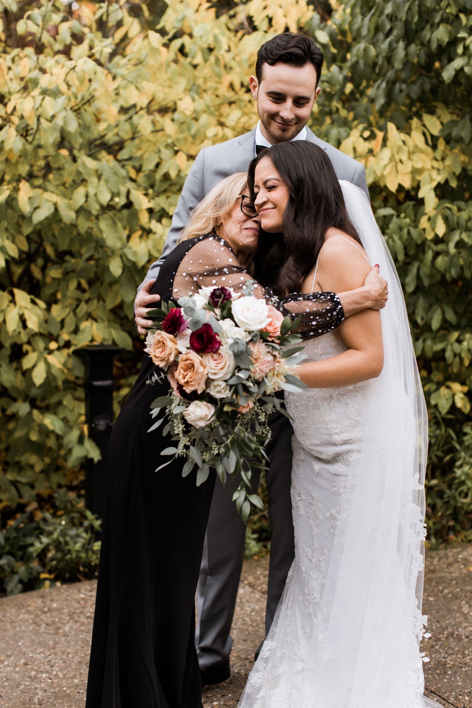 Tender wedding moment captured outdoors with autumn leaves and romantic floral bouquet.