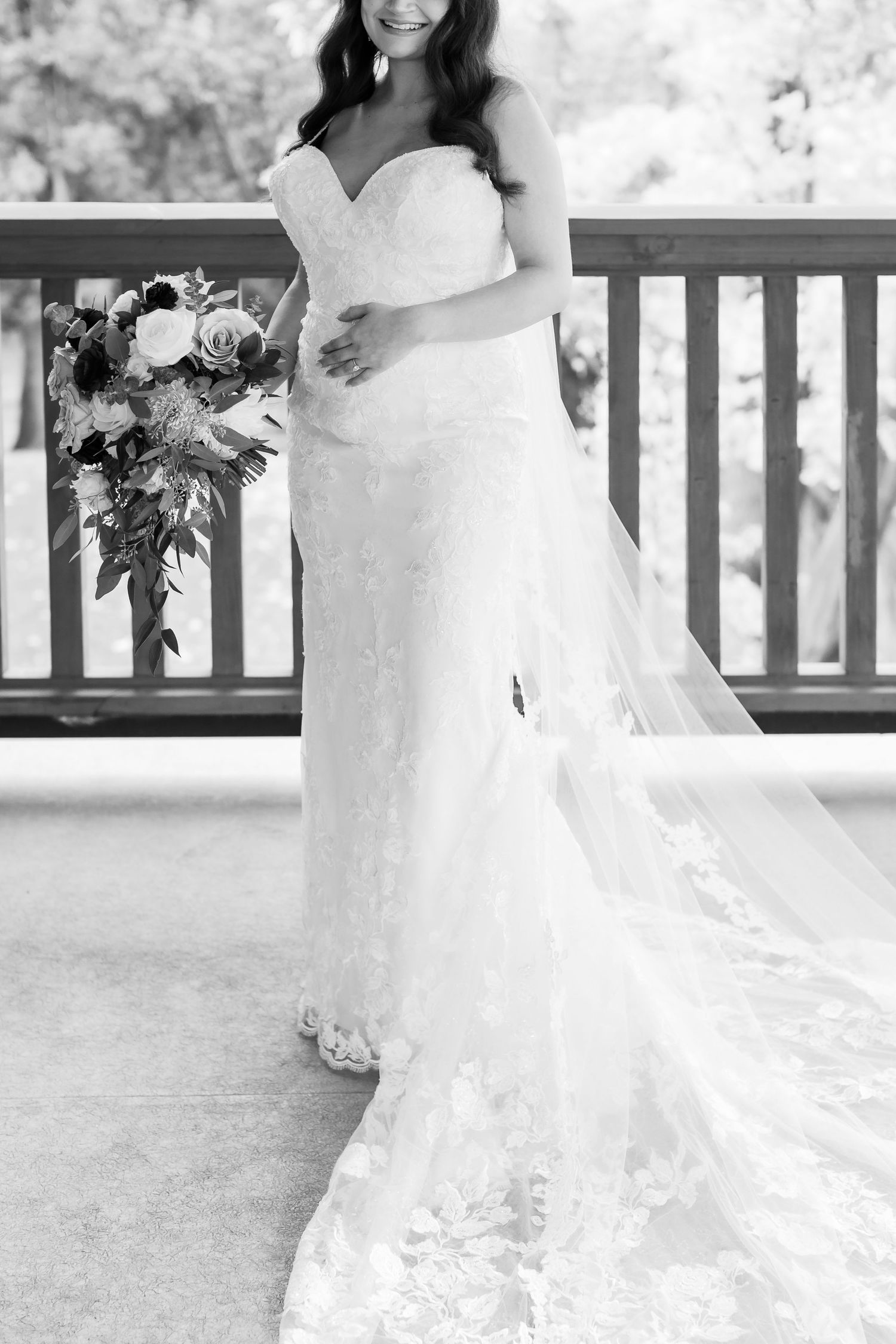Black and white portrait of bride in elegant strapless gown holding floral bouquet.