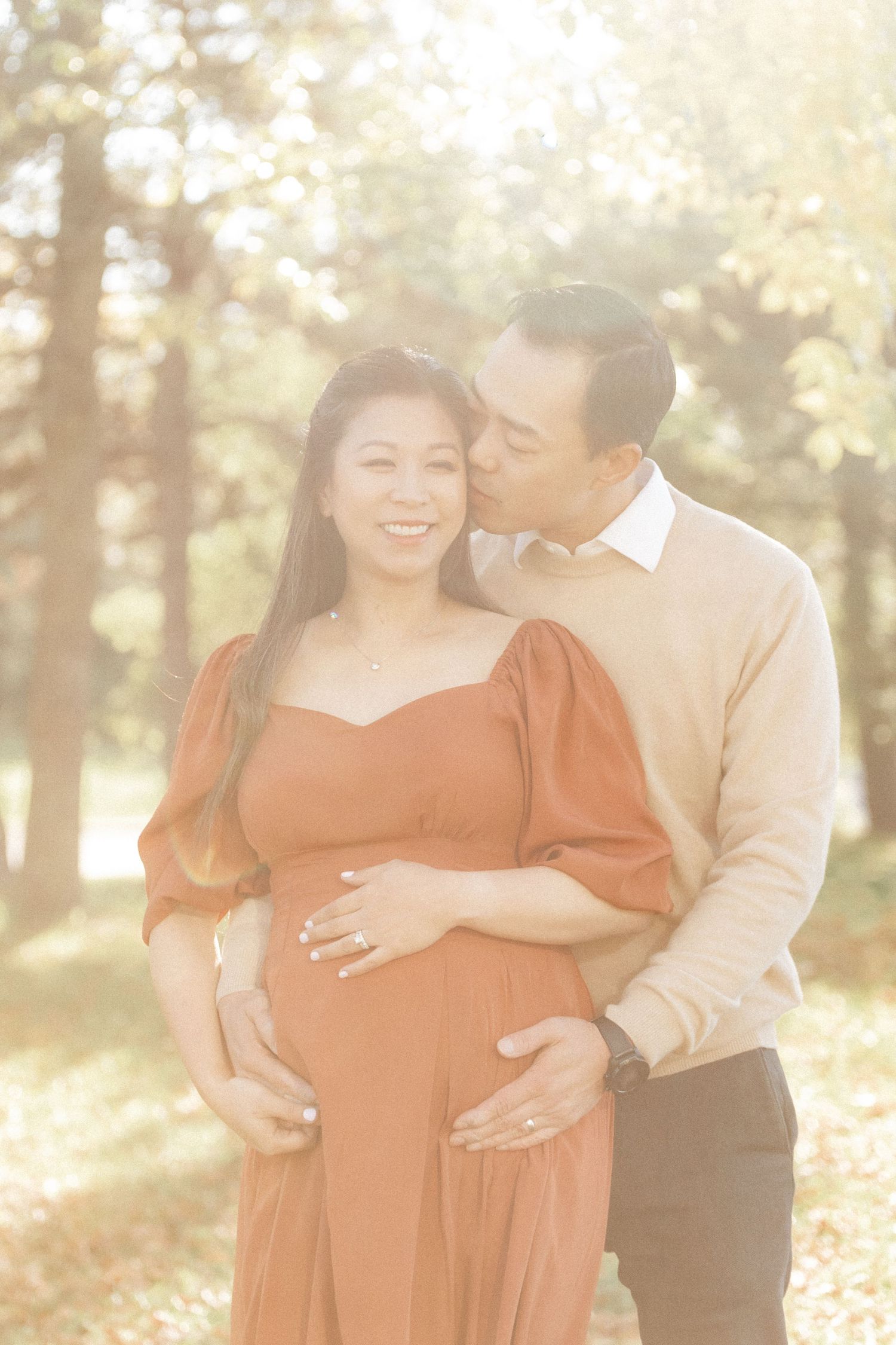 A tender maternity moment captured in golden sunlight with couple in coordinating casual wear.