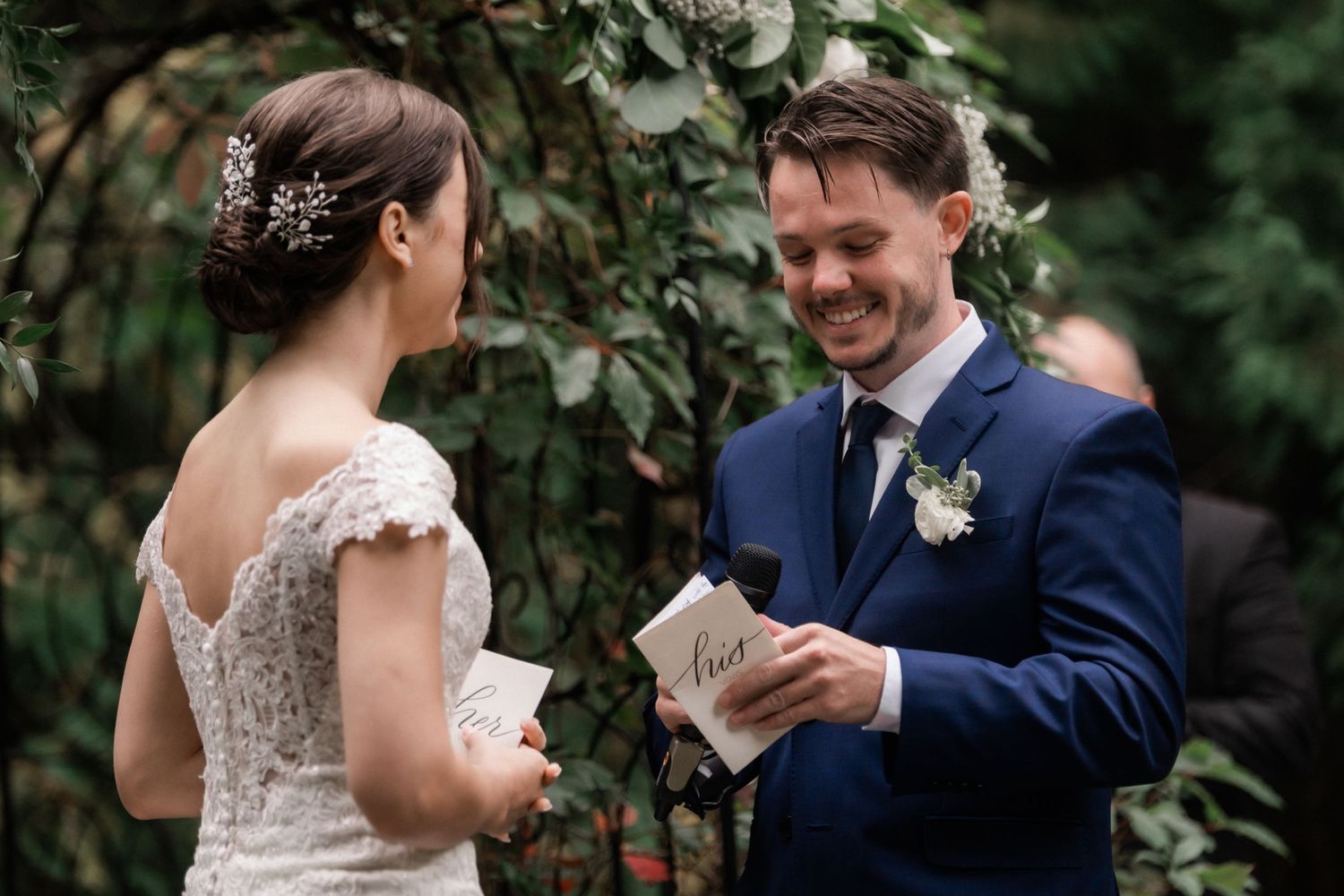 Couple exchanges emotional vows during outdoor garden wedding ceremony under floral archway.