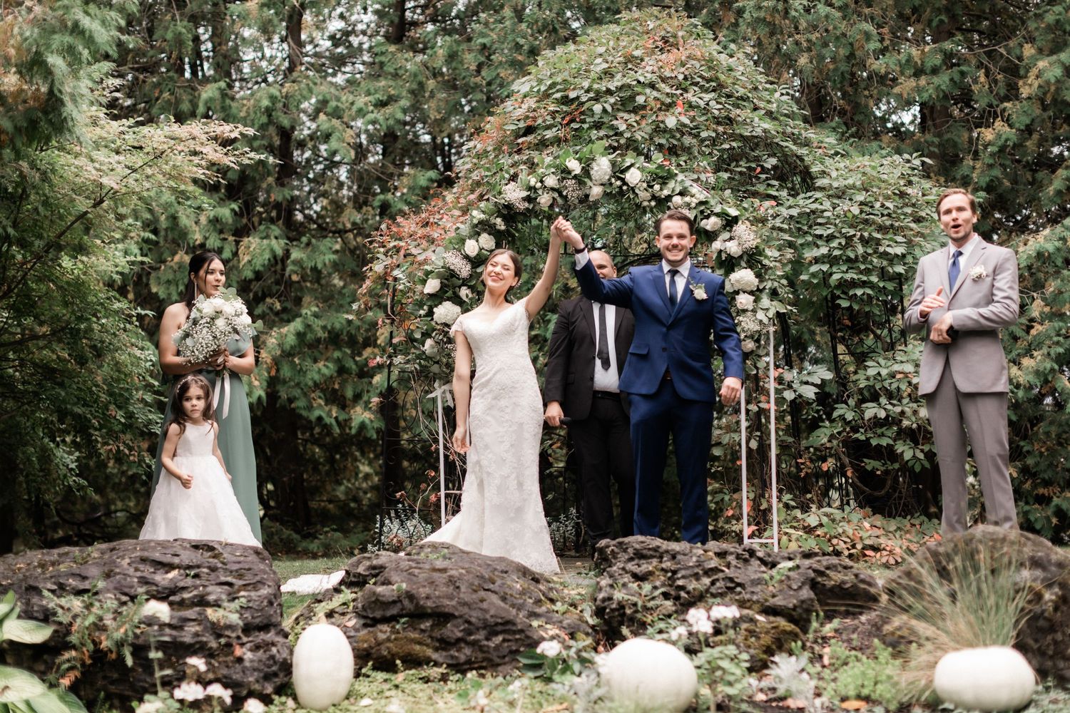 Wedding celebration moment under a garden arch decorated with white flowers and greenery.