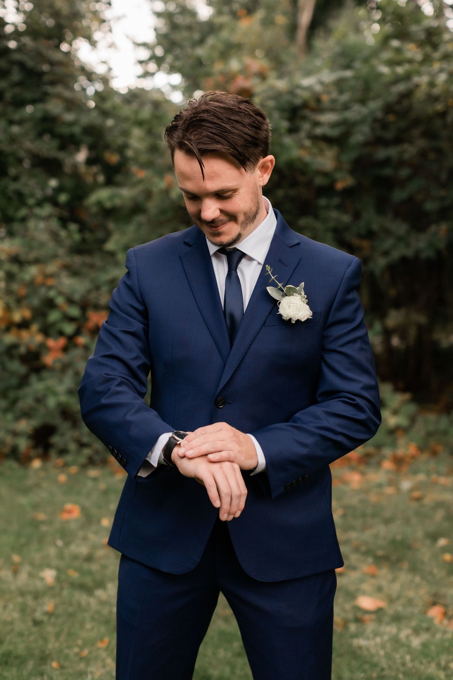 Groom checking watch while wearing tailored navy suit outdoors.