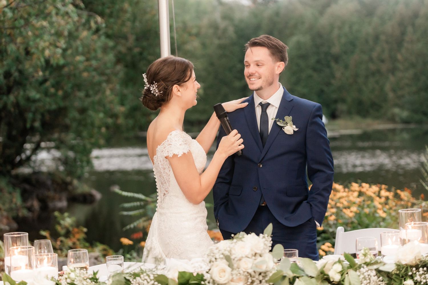 A couple shares a joyful moment at their outdoor wedding reception surrounded by elegant table settings and florals.