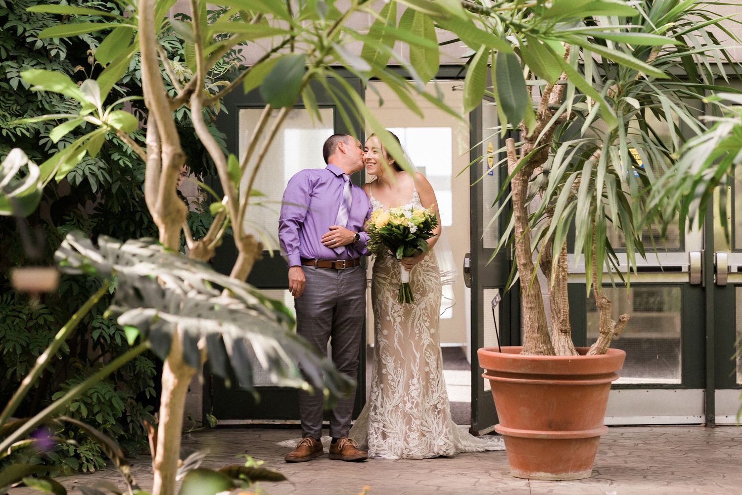 A romantic moment captured between newlyweds in a conservatory setting with tropical plants.