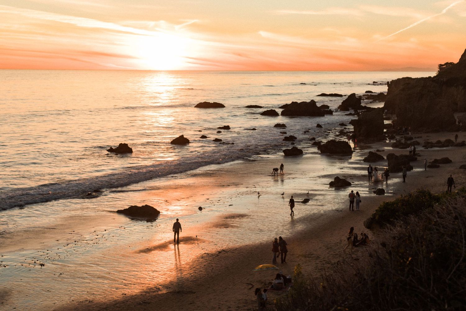 Beautiful sunset beach scene with people walking along rocky coastline.