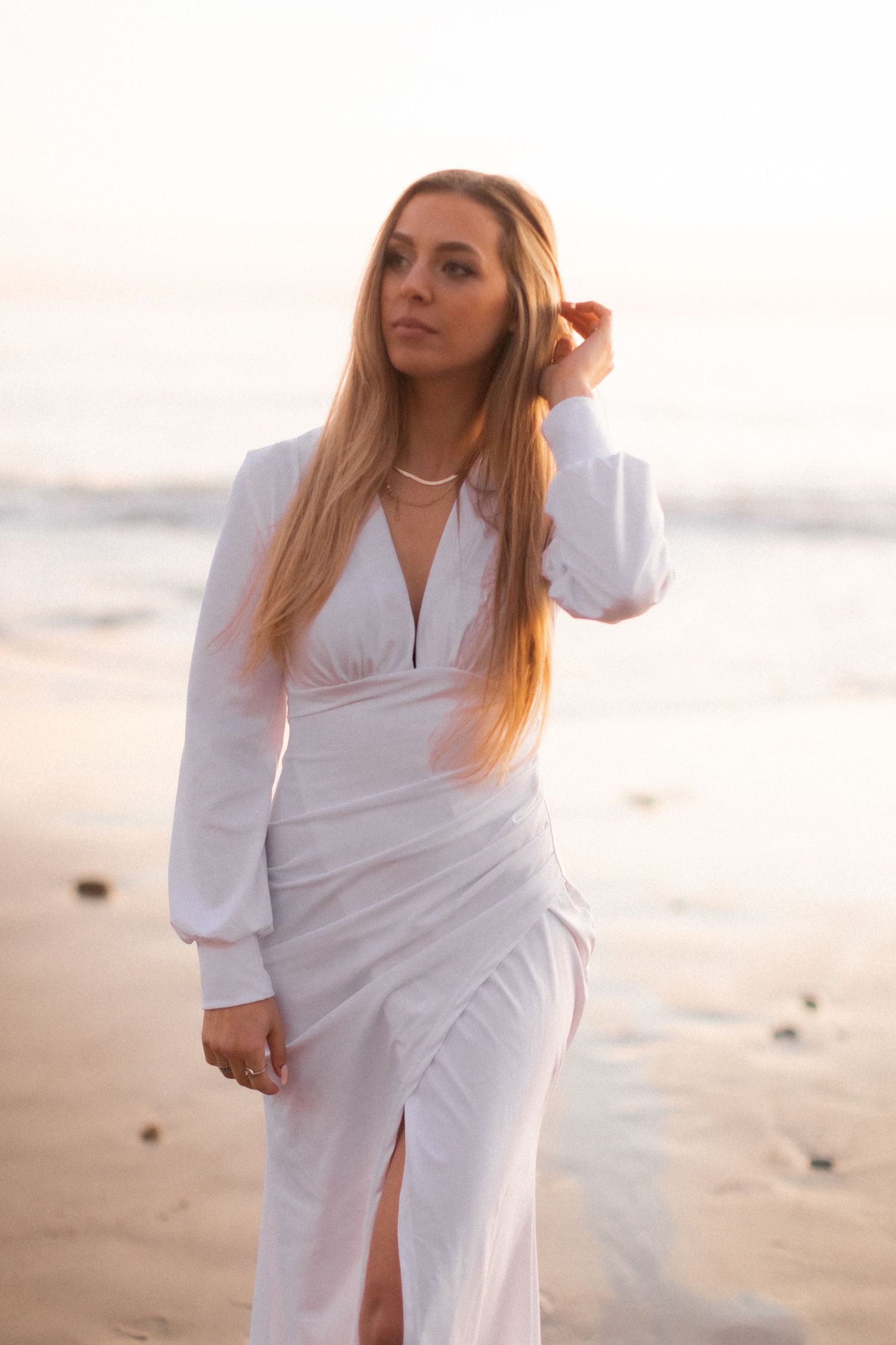 Woman in white dress posing on beach at sunset.