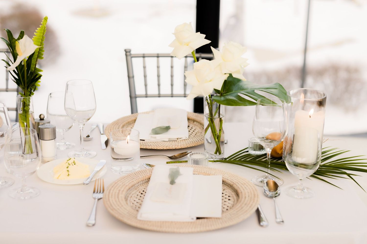 Elegant table setting with white linens, palm leaves and crystal glassware at a wedding reception.