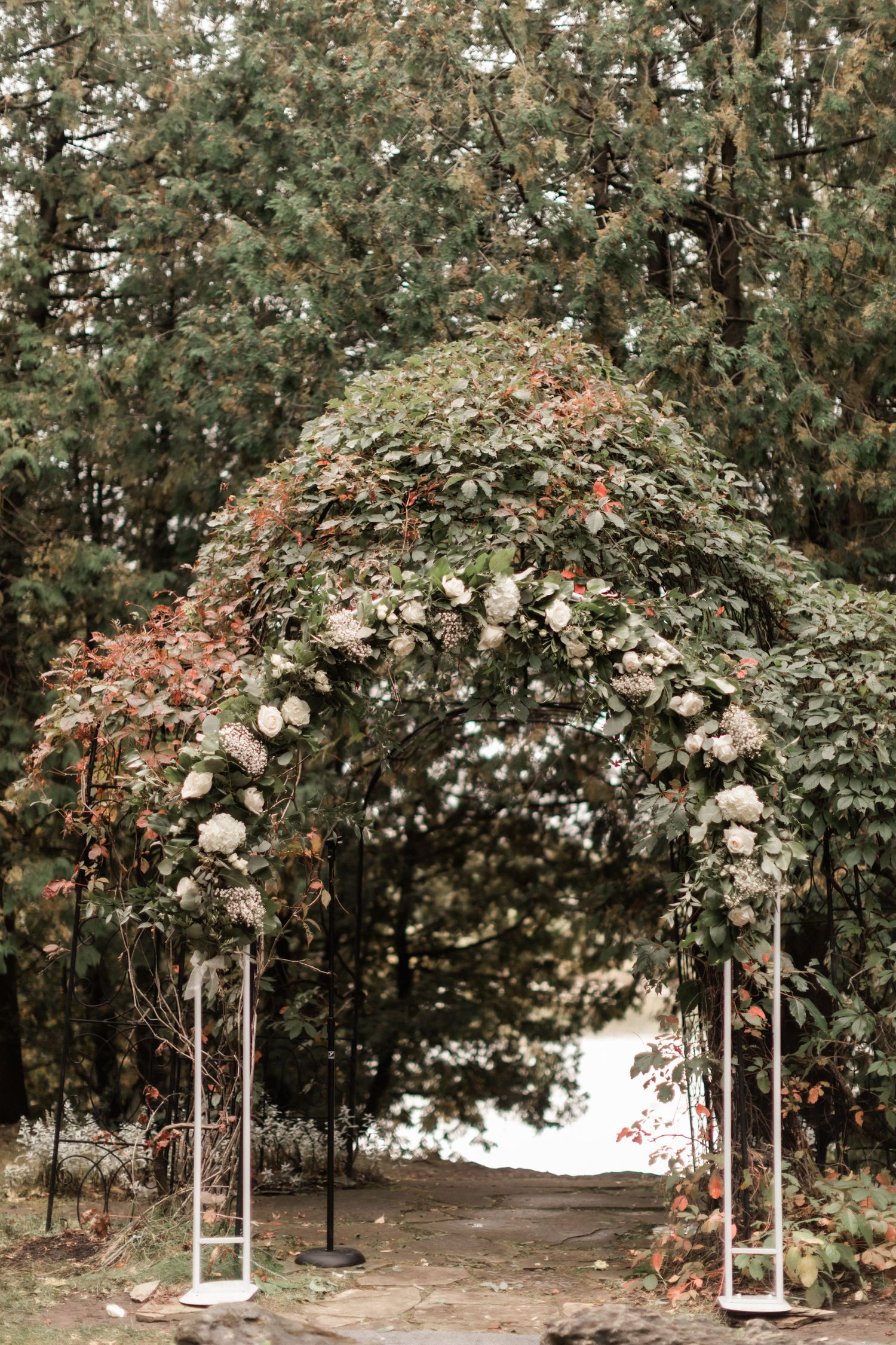 Garden archway adorned with white roses and greenery creating romantic wedding ceremony backdrop.