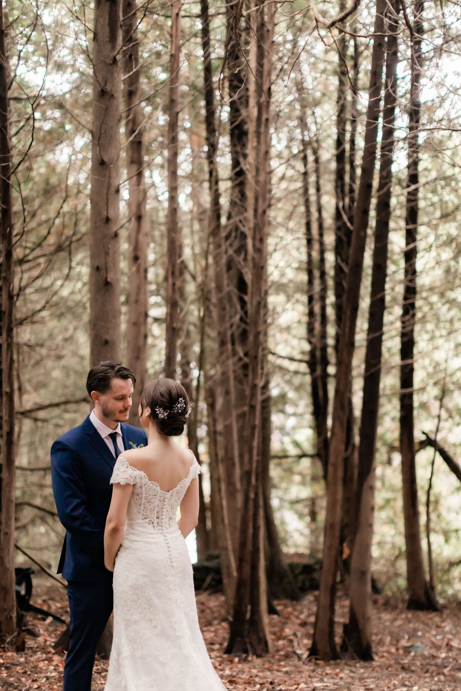 Elegant wedding portrait showcasing detailed back of lace wedding dress in forest setting.