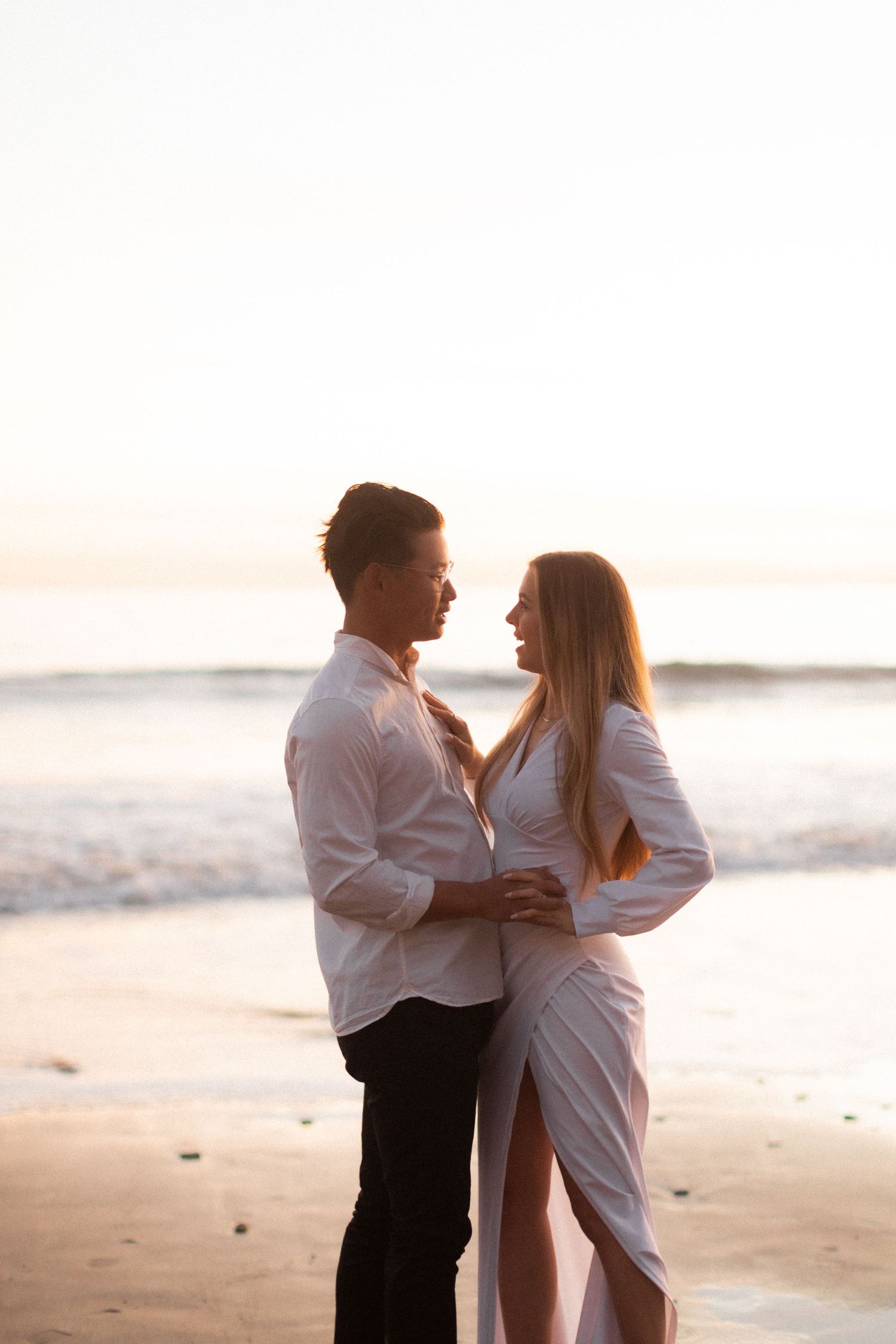 Couple embracing on beach during sunset wearing coordinated white and black outfits.