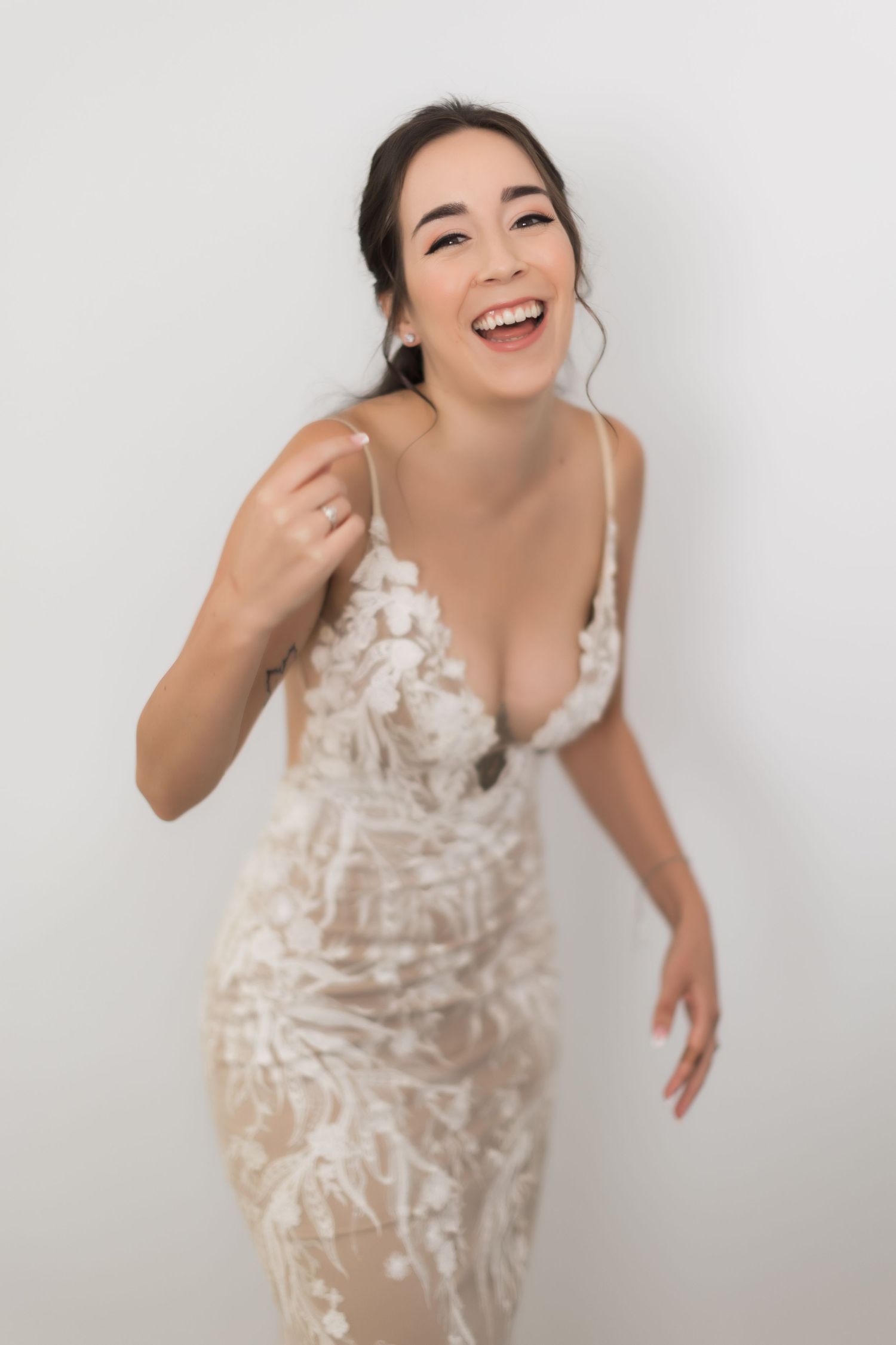 Woman in fitted lace wedding dress laughs expressively during photo session.