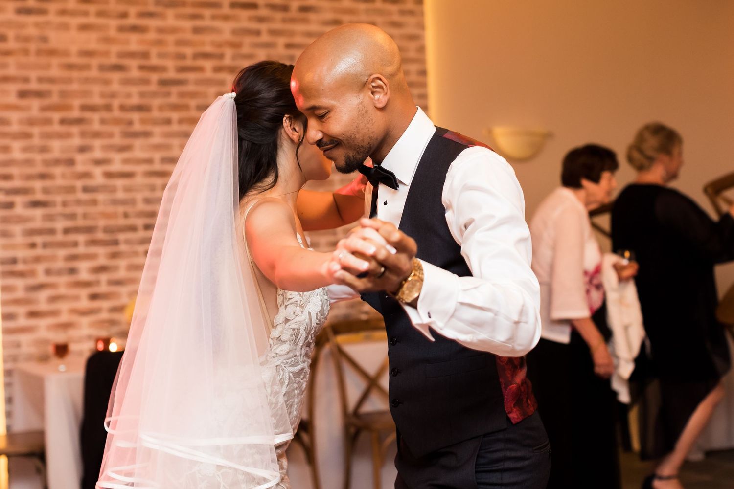 A couple shares an intimate dance moment against exposed brick walls at their wedding reception.
