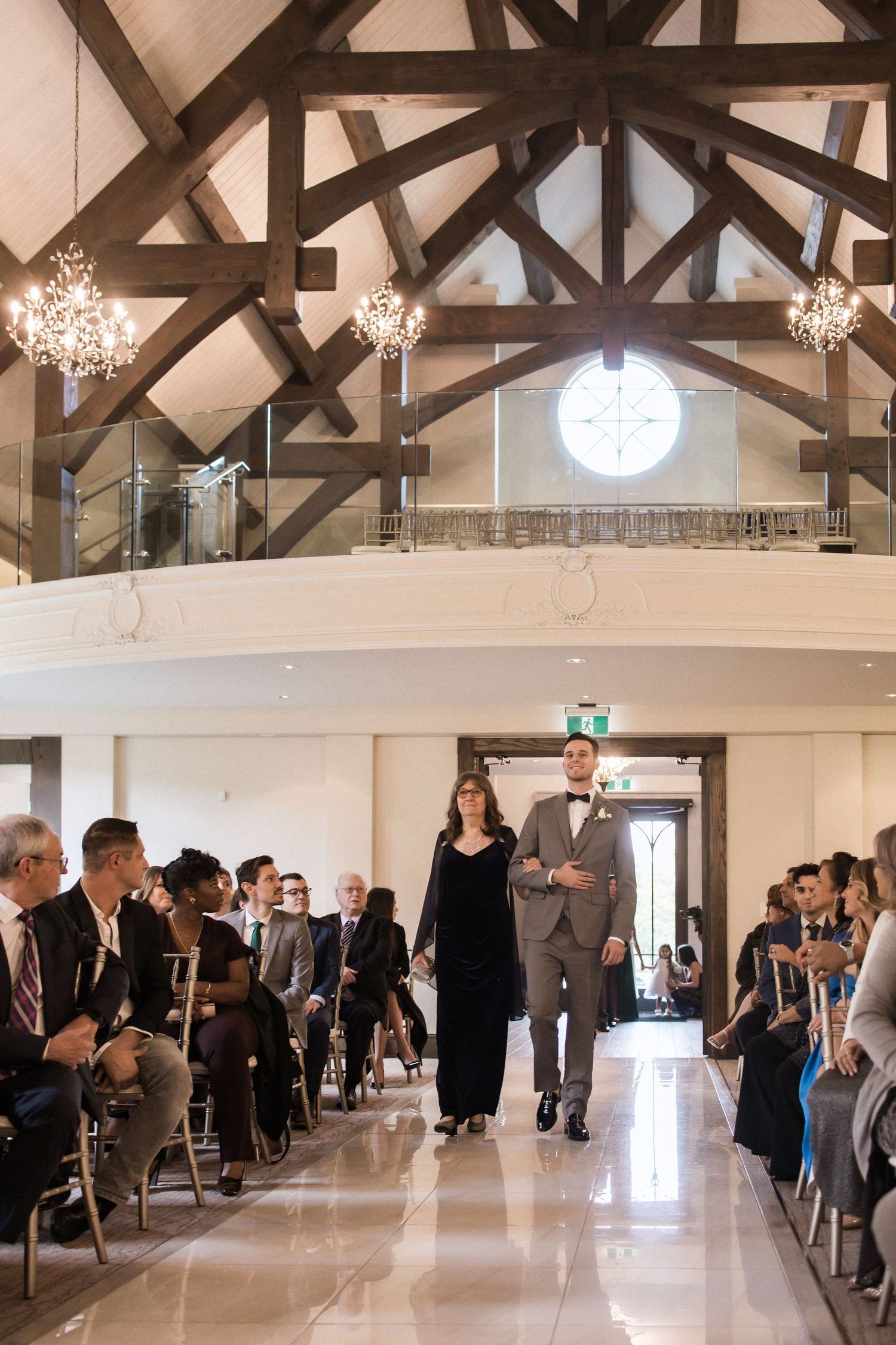 Wedding ceremony processional in an elegant chapel with exposed wooden beams and crystal chandeliers.