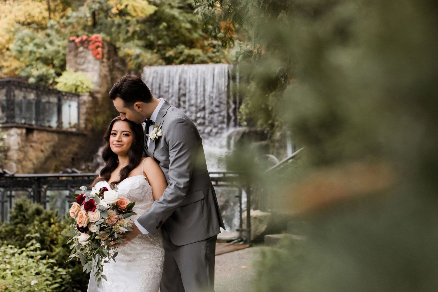 Intimate wedding portrait with couple embracing against blurred autumn foliage.