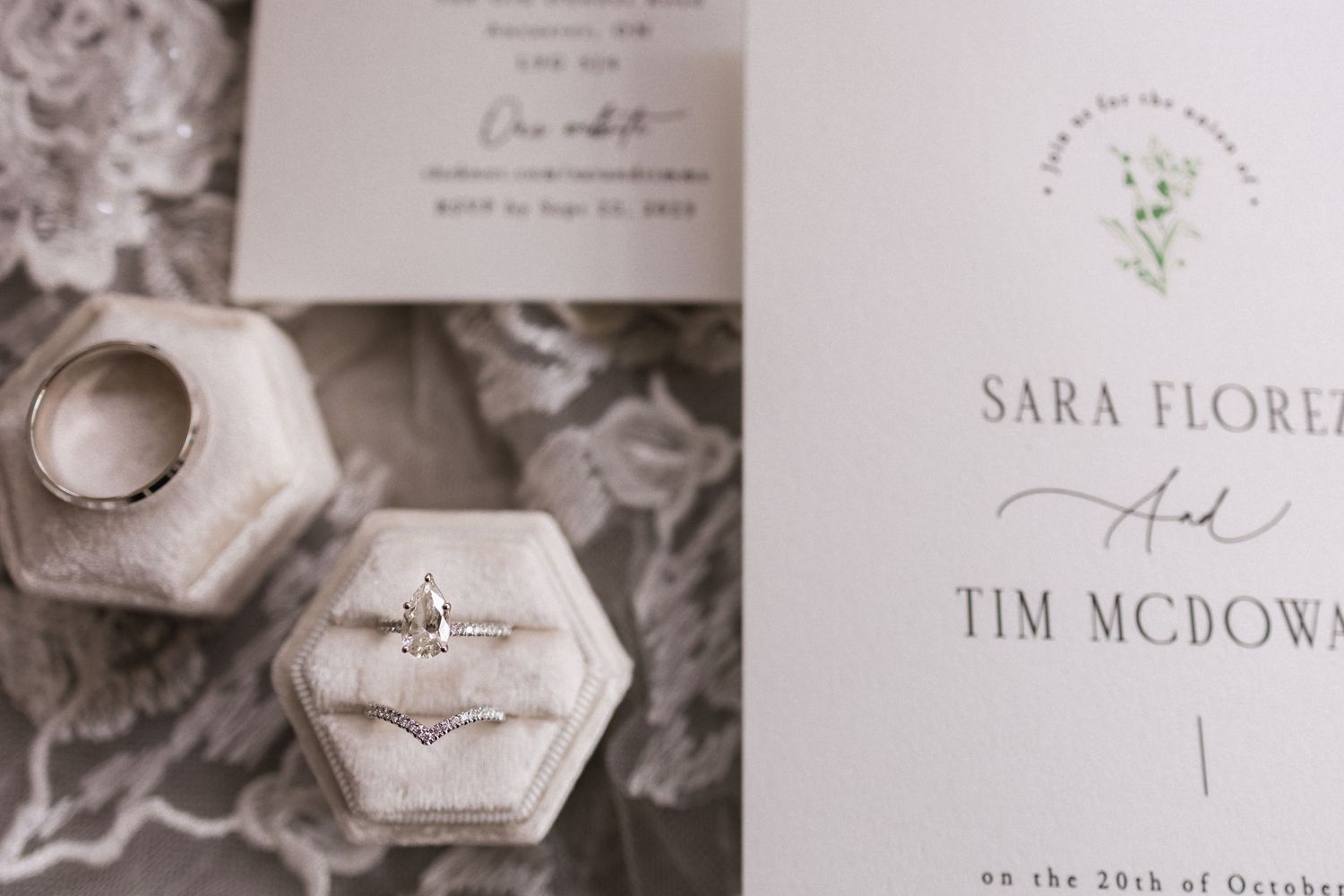 Wedding invitation and hexagonal ring boxes containing wedding rings displayed on a textured surface.