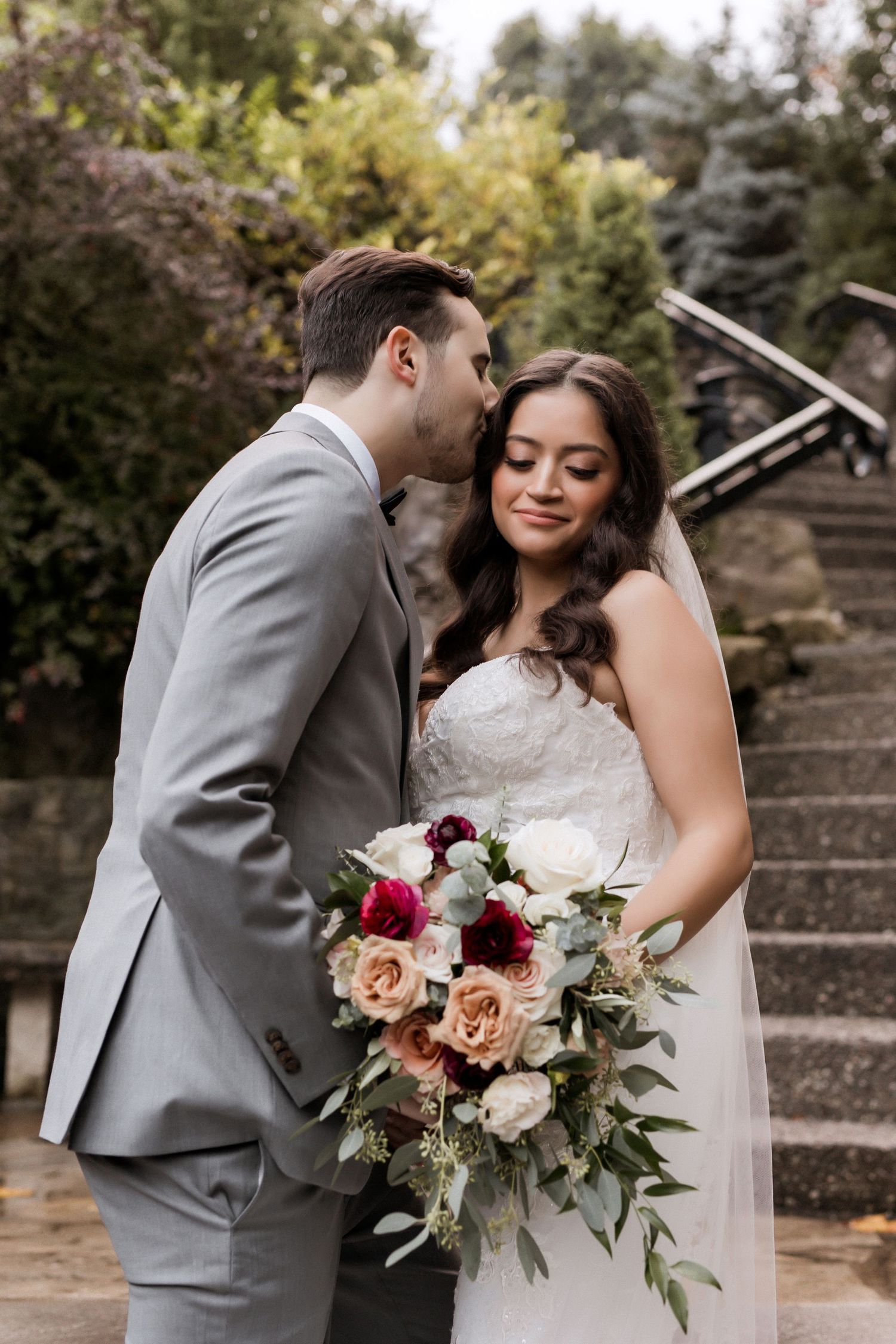 Intimate wedding portrait with beautiful bouquet of roses and greenery on stone staircase.