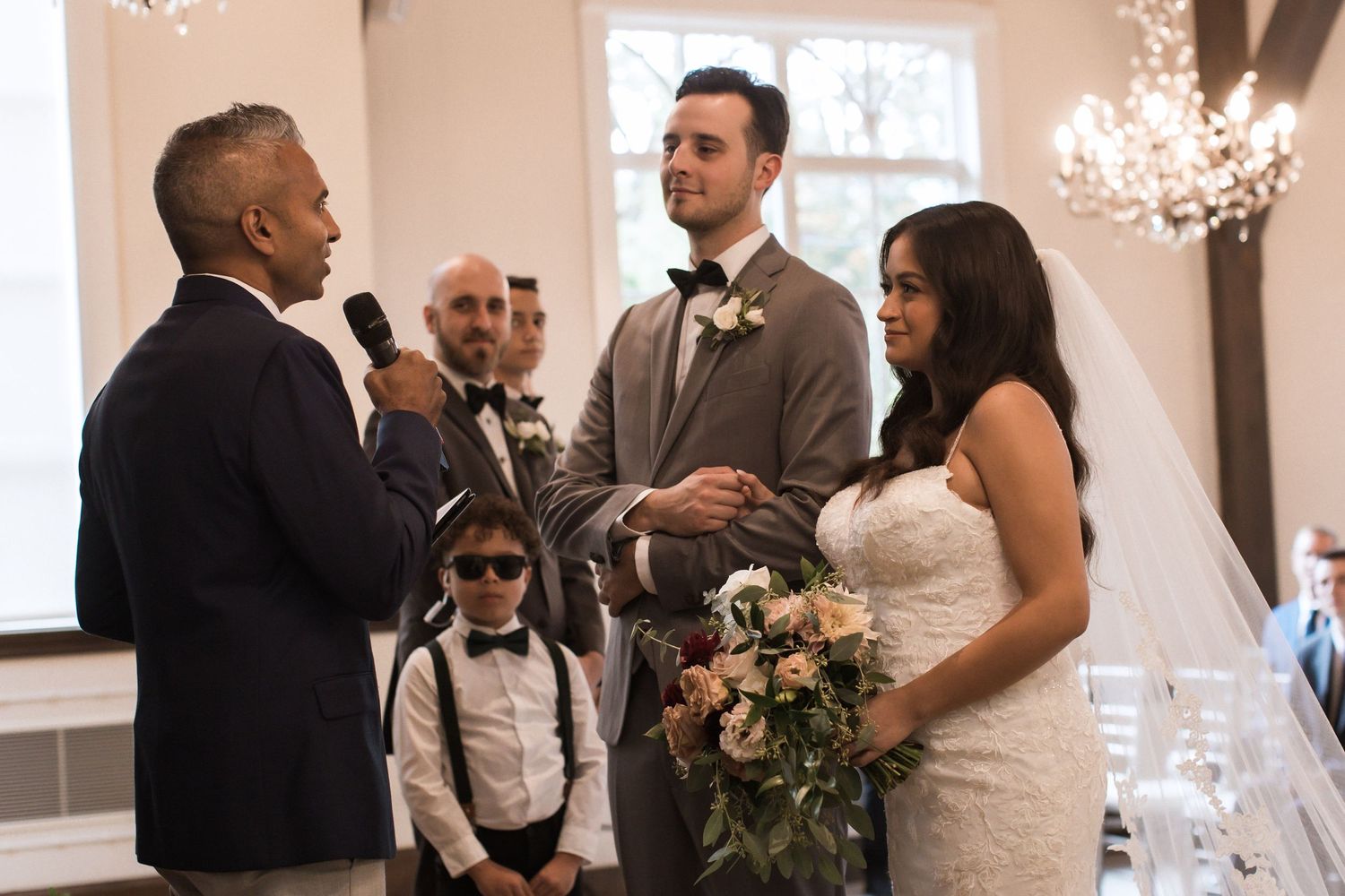A wedding ceremony taking place in an elegant room with chandeliers as a couple exchanges vows at the altar.