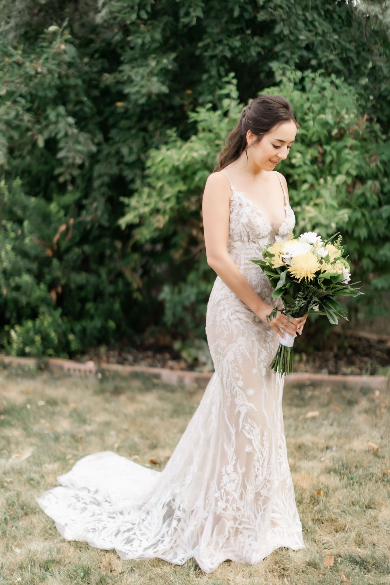 A stunning bridal portrait outdoors featuring a fitted lace gown and yellow bouquet.