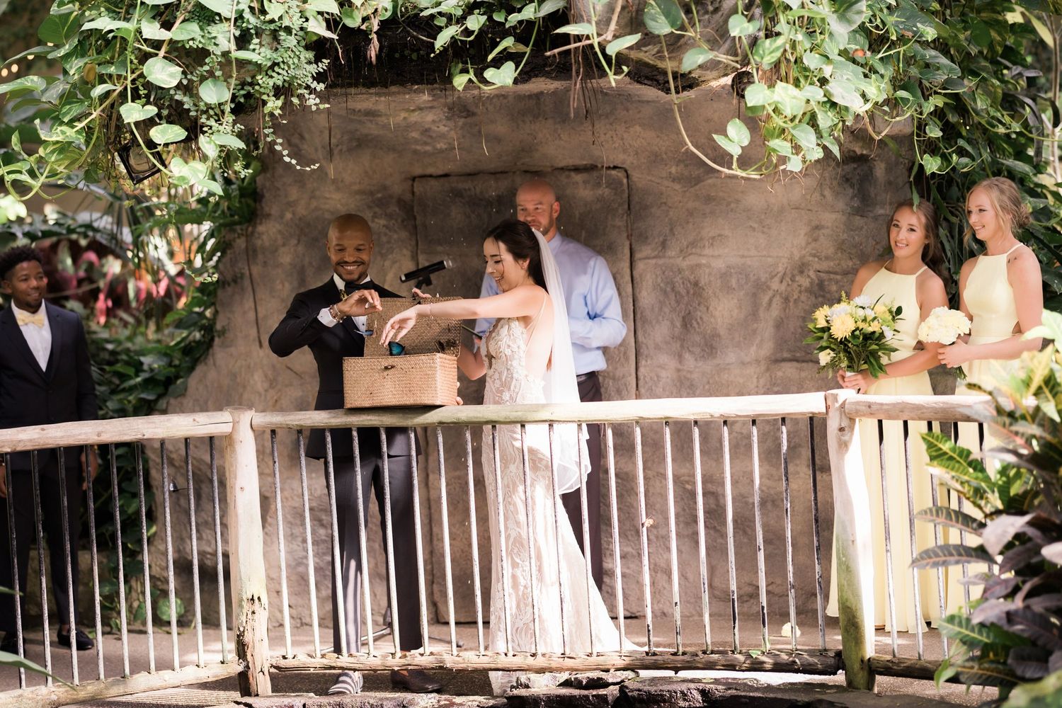 Wedding ceremony taking place in rustic stone venue with greenery and white railings.