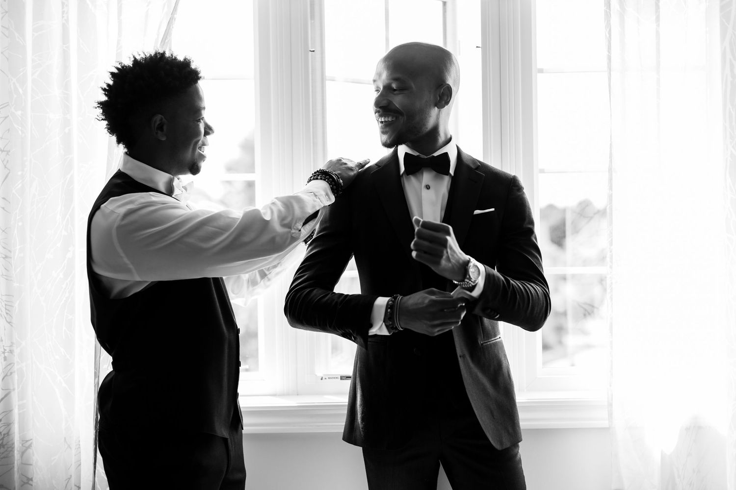 A black and white shot of formal wear adjustments being made near a window.