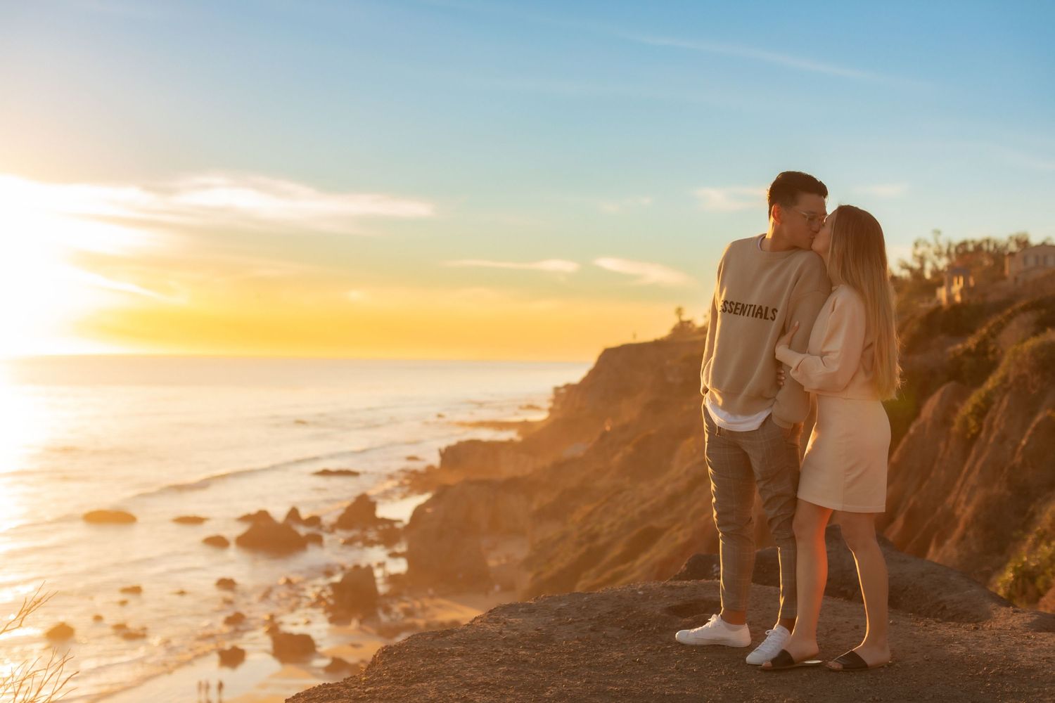 Couple stands together on rocky overlook watching dramatic ocean sunset.
