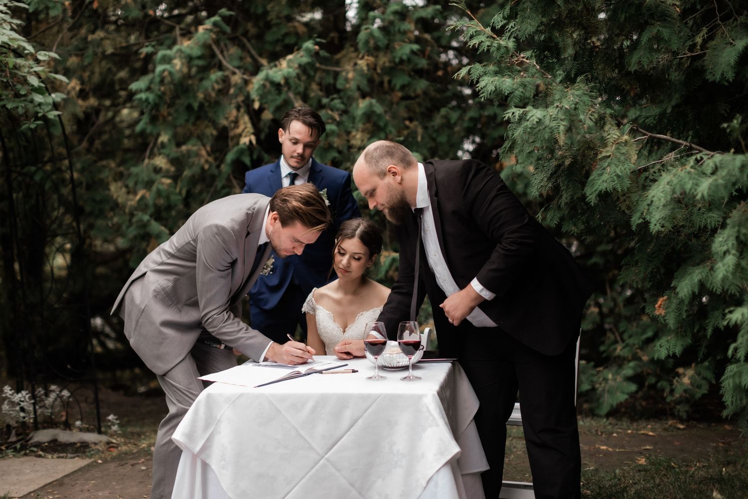 Wedding ceremony document signing at a white-clothed table in an outdoor garden setting.