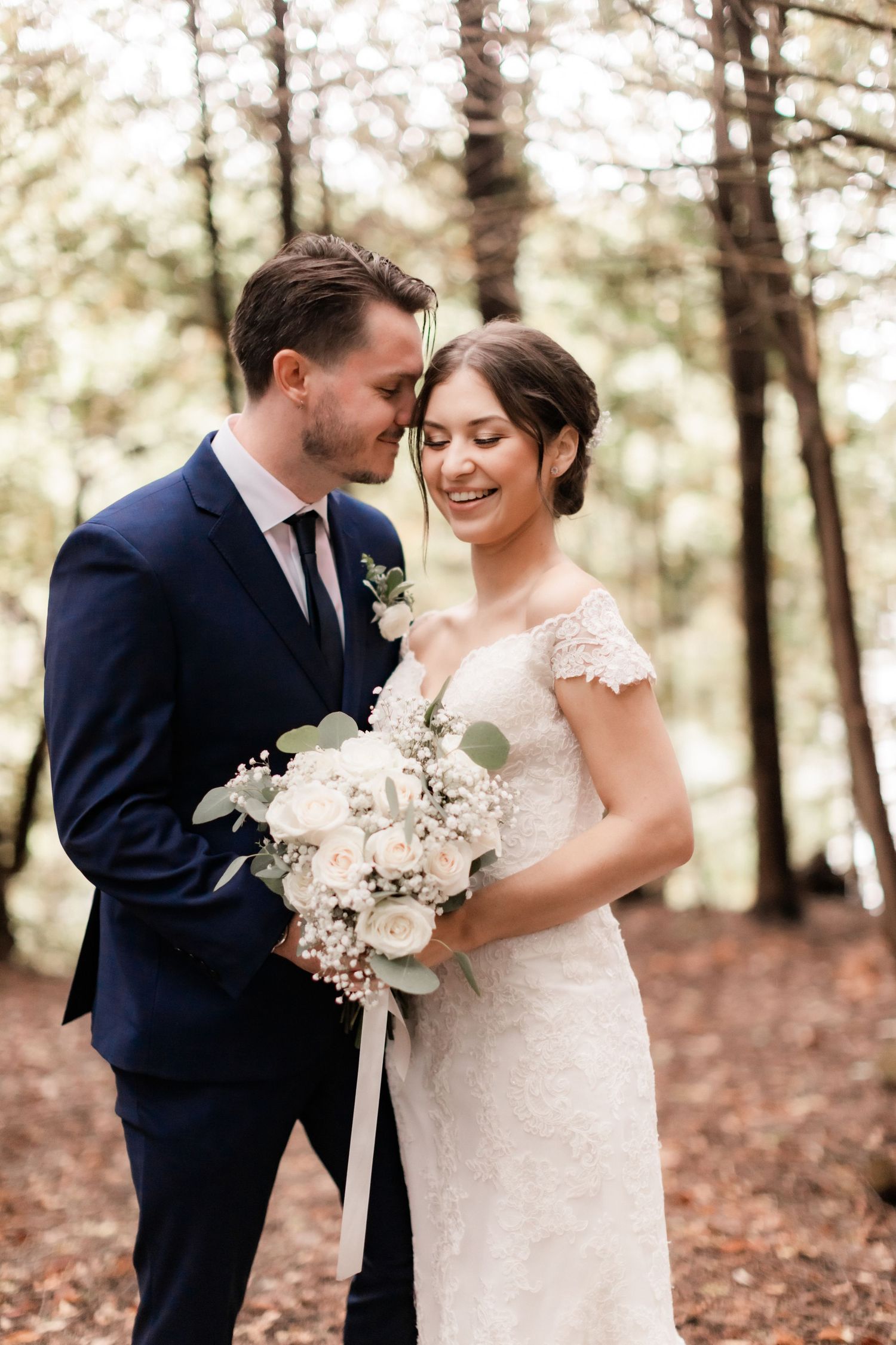 Intimate forest wedding portrait with white floral bouquet and natural woodland backdrop.