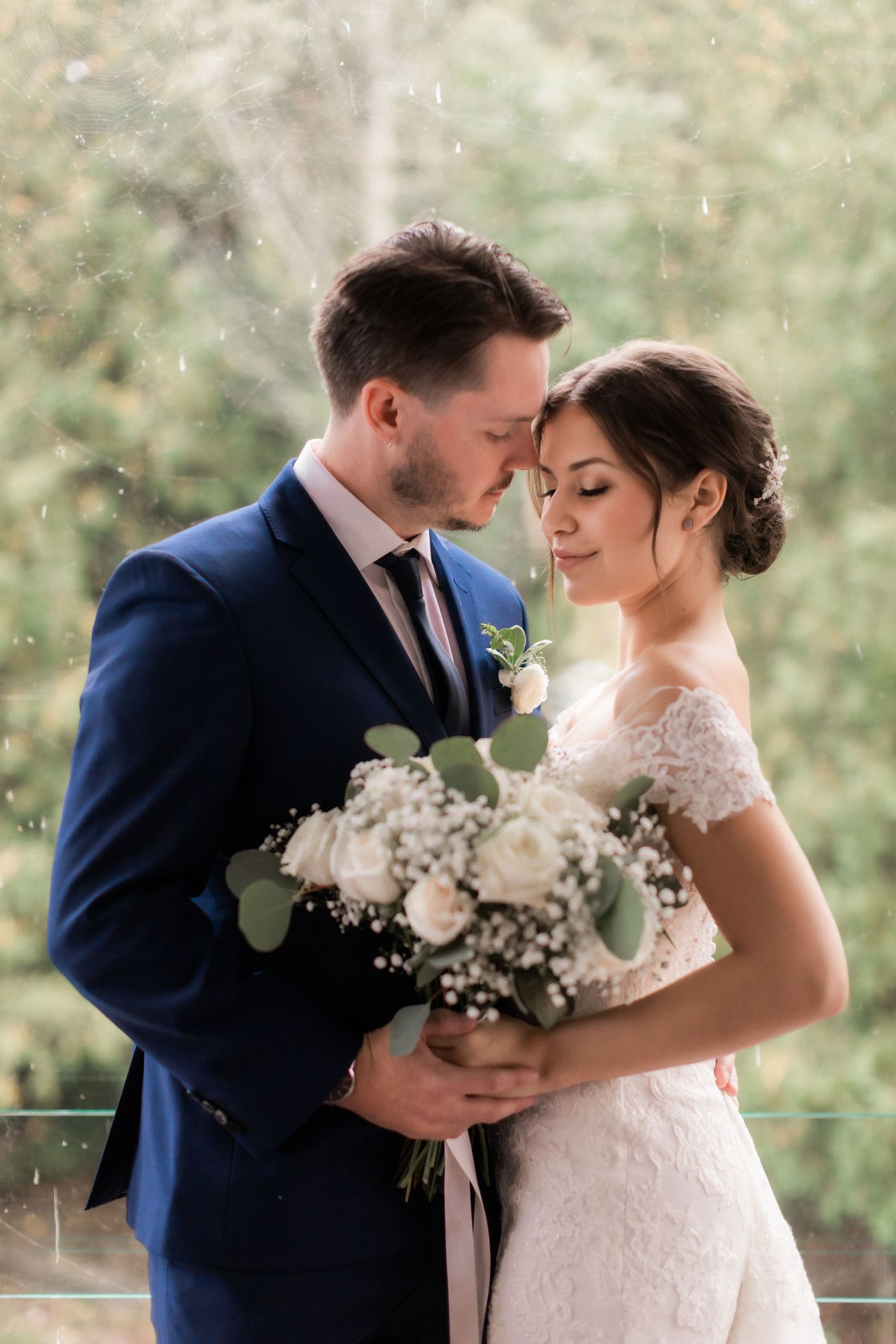 A romantic wedding portrait showing a tender moment with white floral bouquet against a nature backdrop.